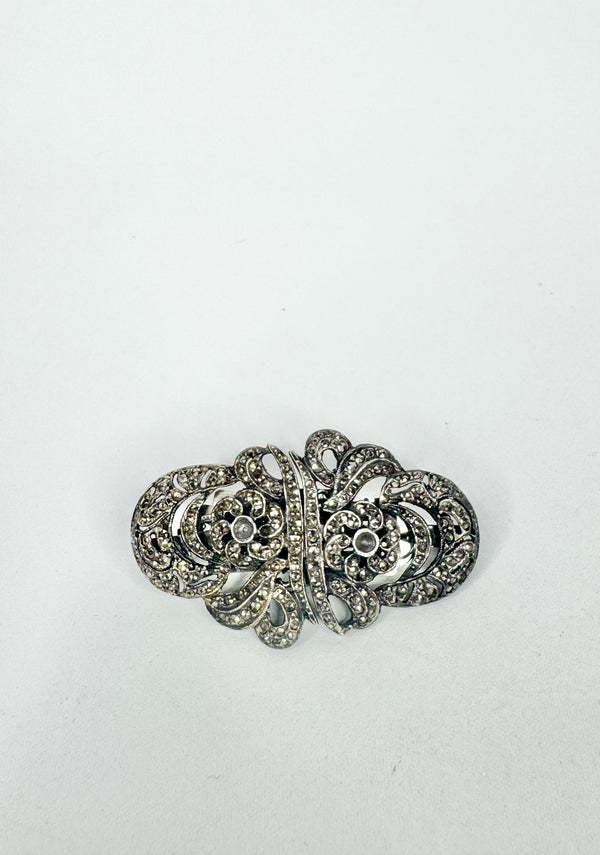 Silver brooch with intricate design on a white background