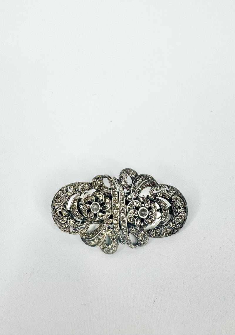 Silver brooch with intricate design on a white background