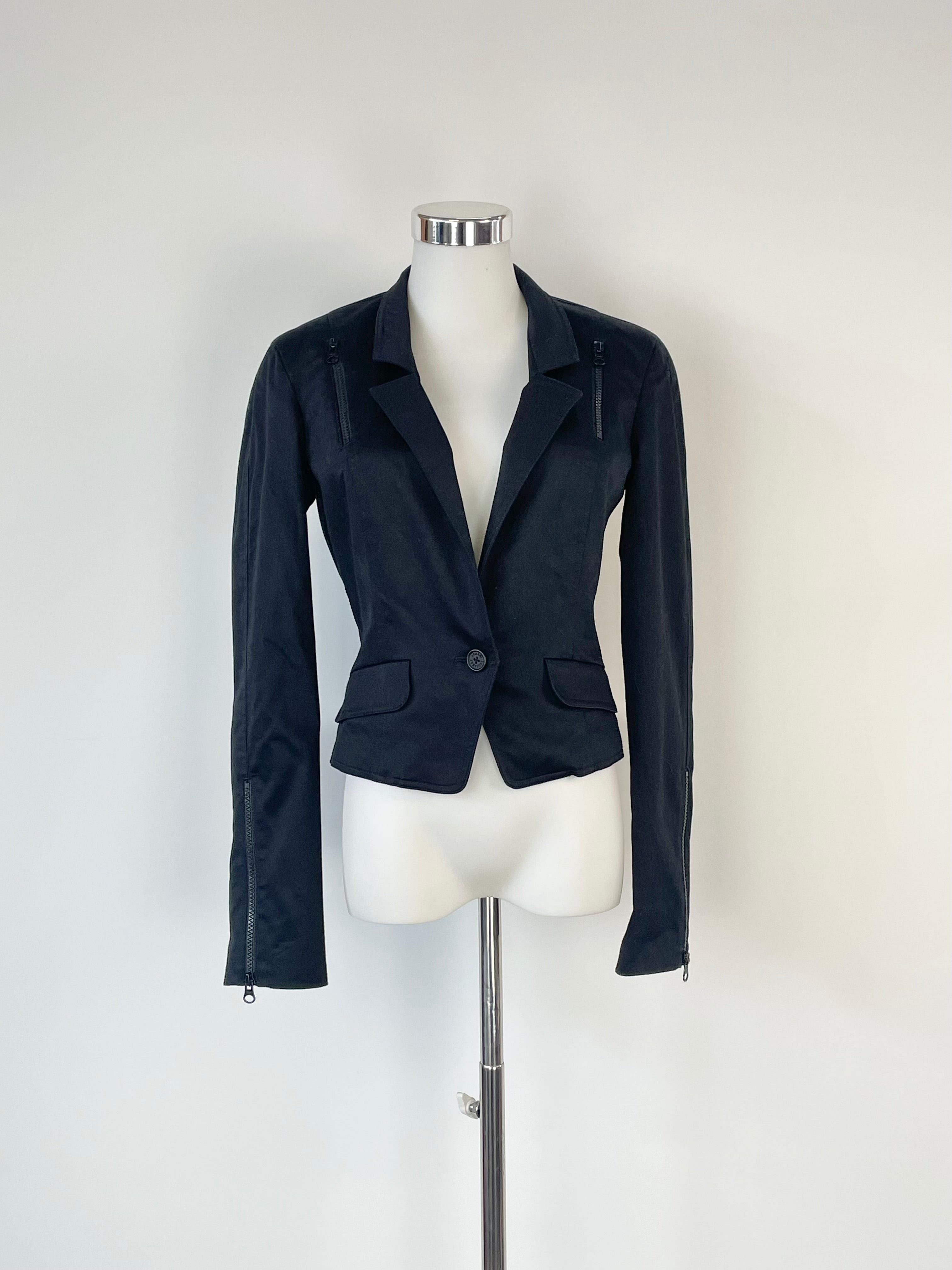A black cropped industrial-style blazer with zippers, displayed on a mannequin against a white background.