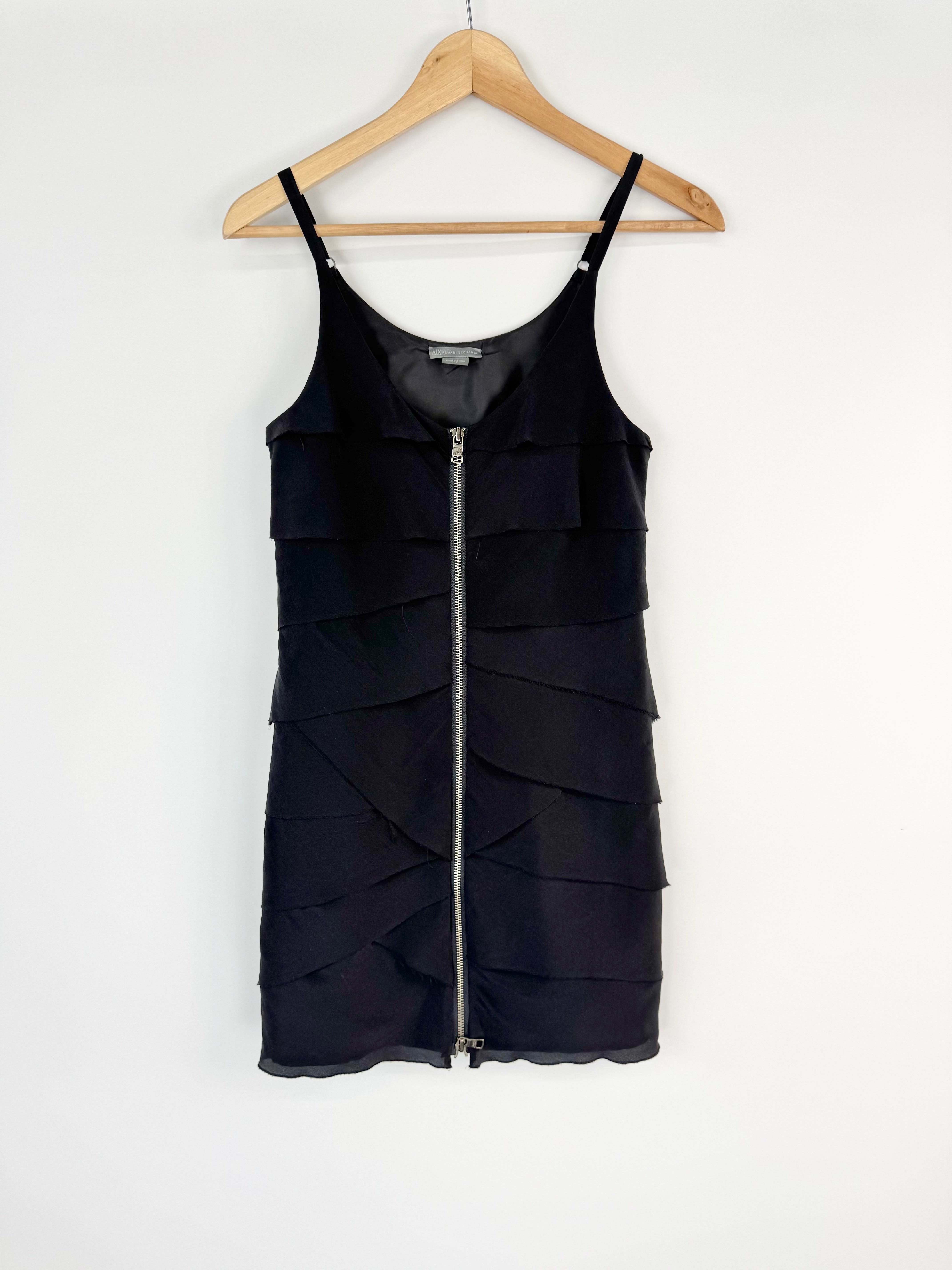 Black tiered dress with a zipper on a wooden hanger against a white background