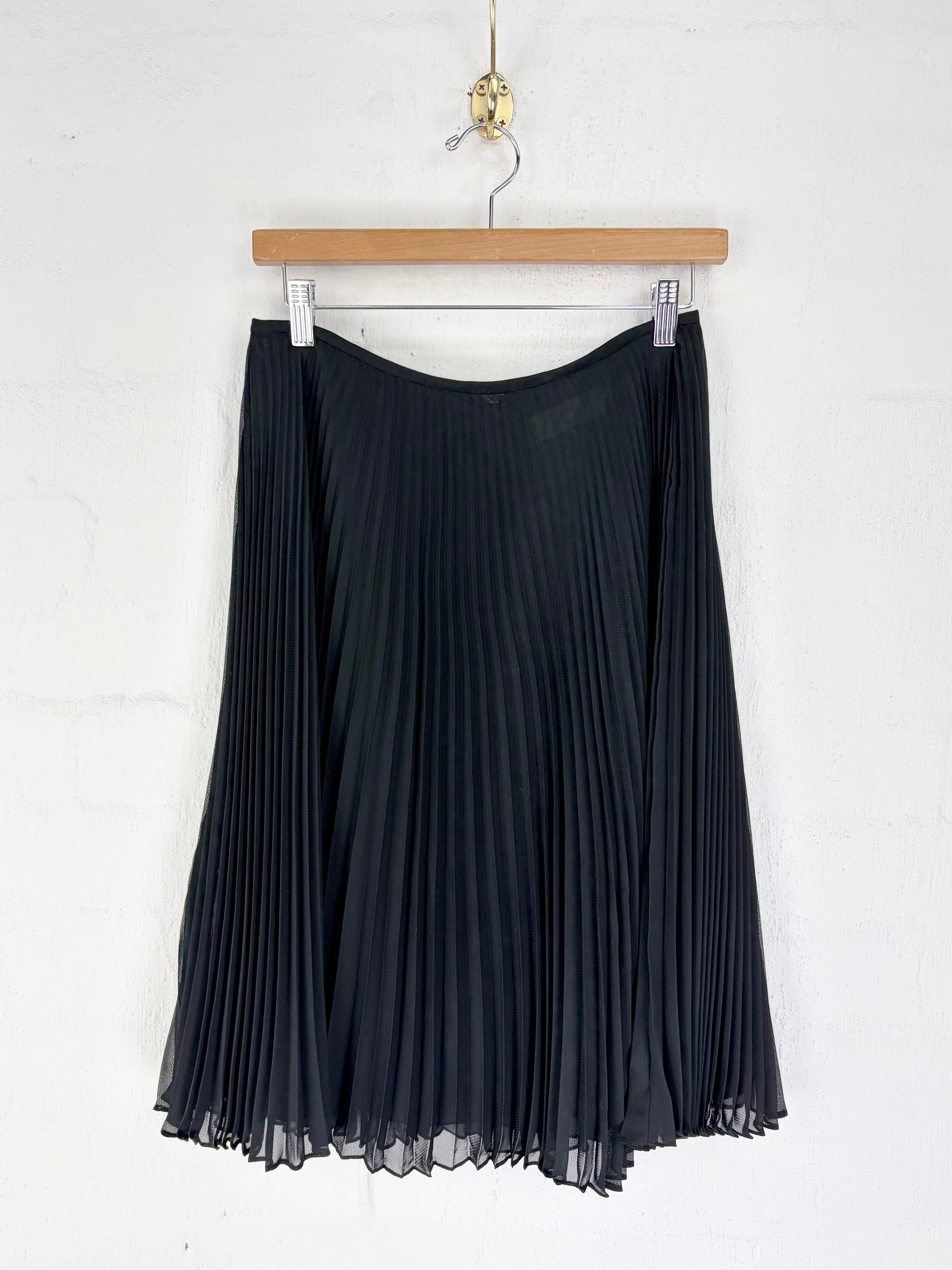 A black pleated skirt hanging from a wooden hanger against a white wall.