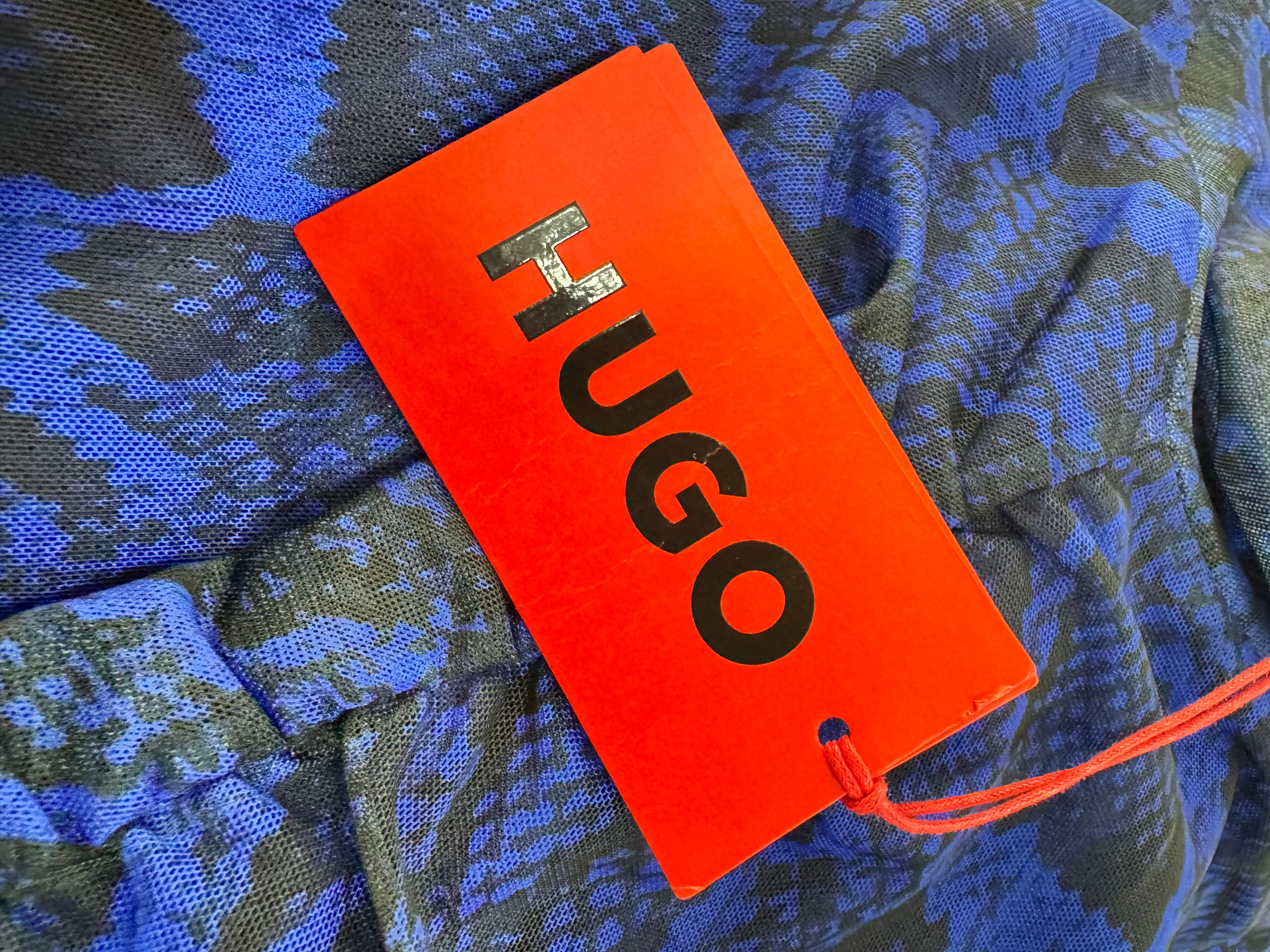 Orange tag with 'HUGO' text on a blue camouflage fabric background