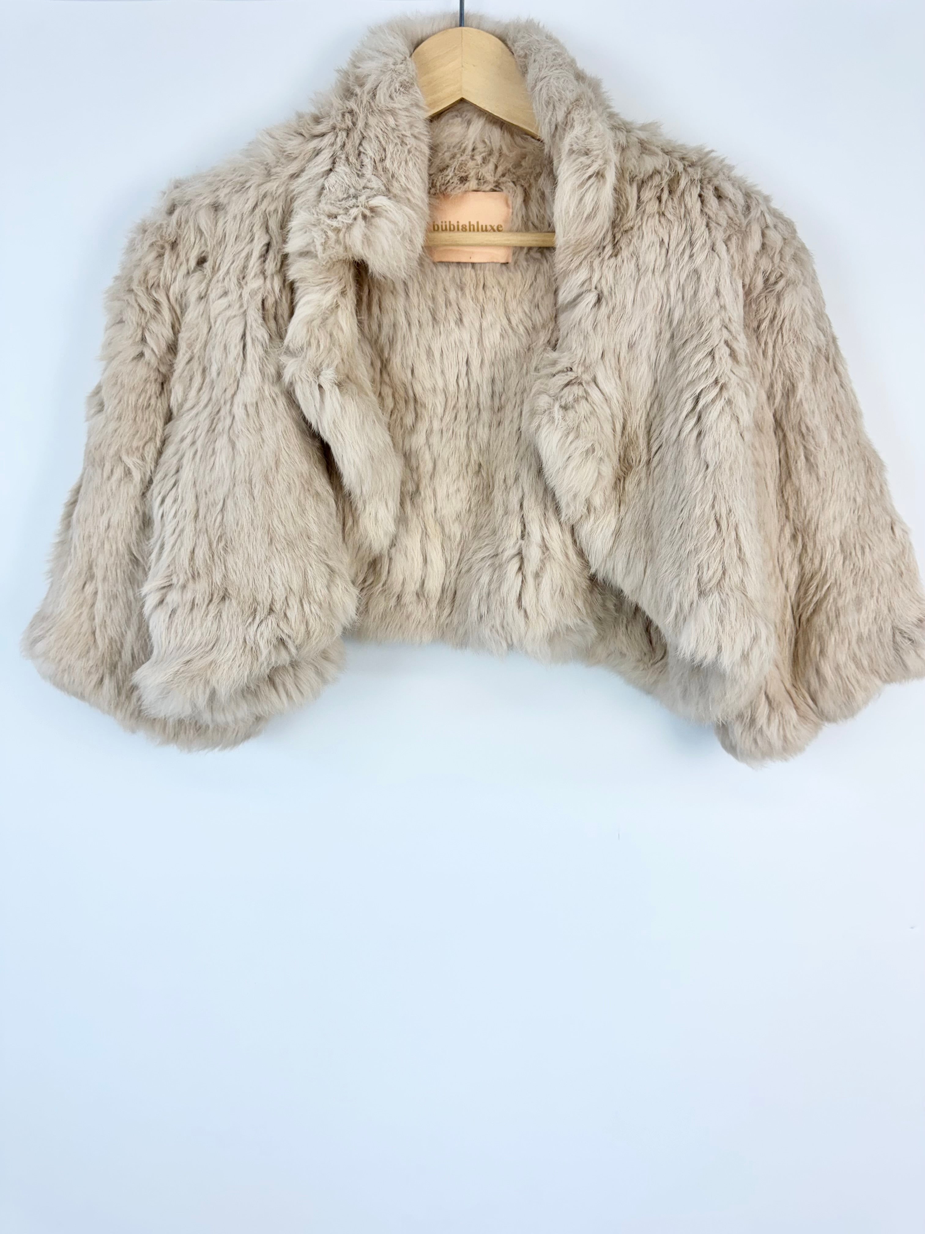 Beige faux fur jacket on a wooden hanger against a white background