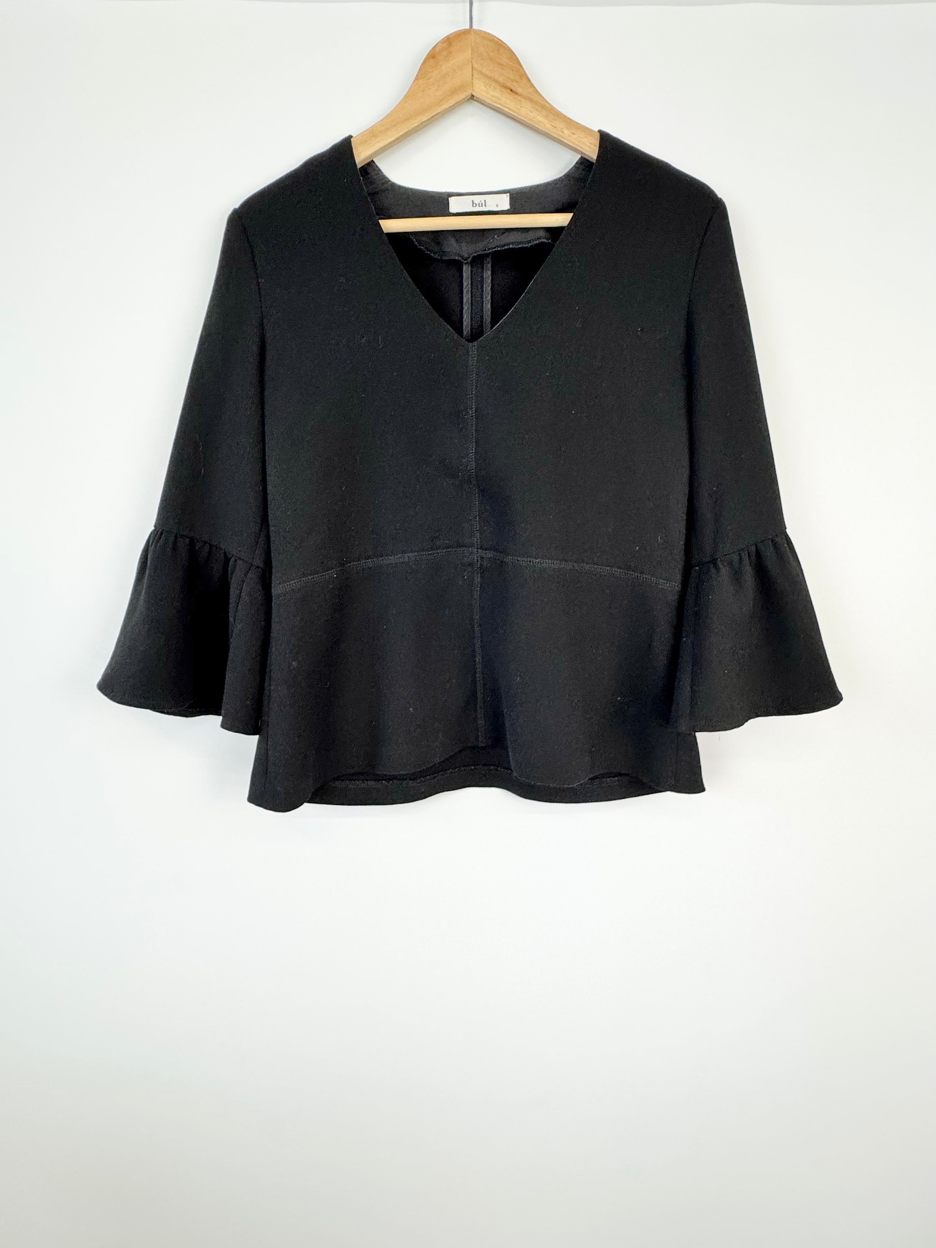 Black blouse with ruffled sleeves on a wooden hanger against a white background