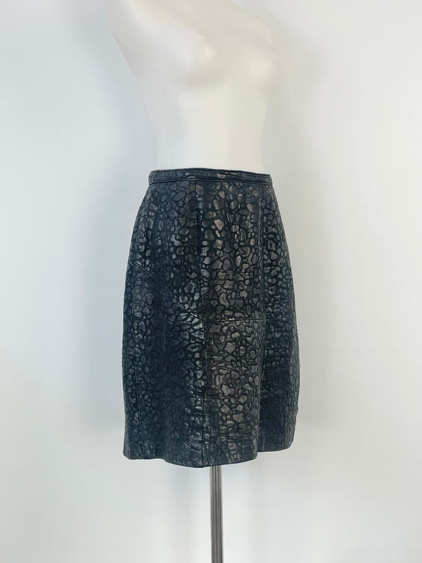 A black leather textured midi skirt displayed on a mannequin, featuring a subtle animal print and a rayon lining visible at the base.