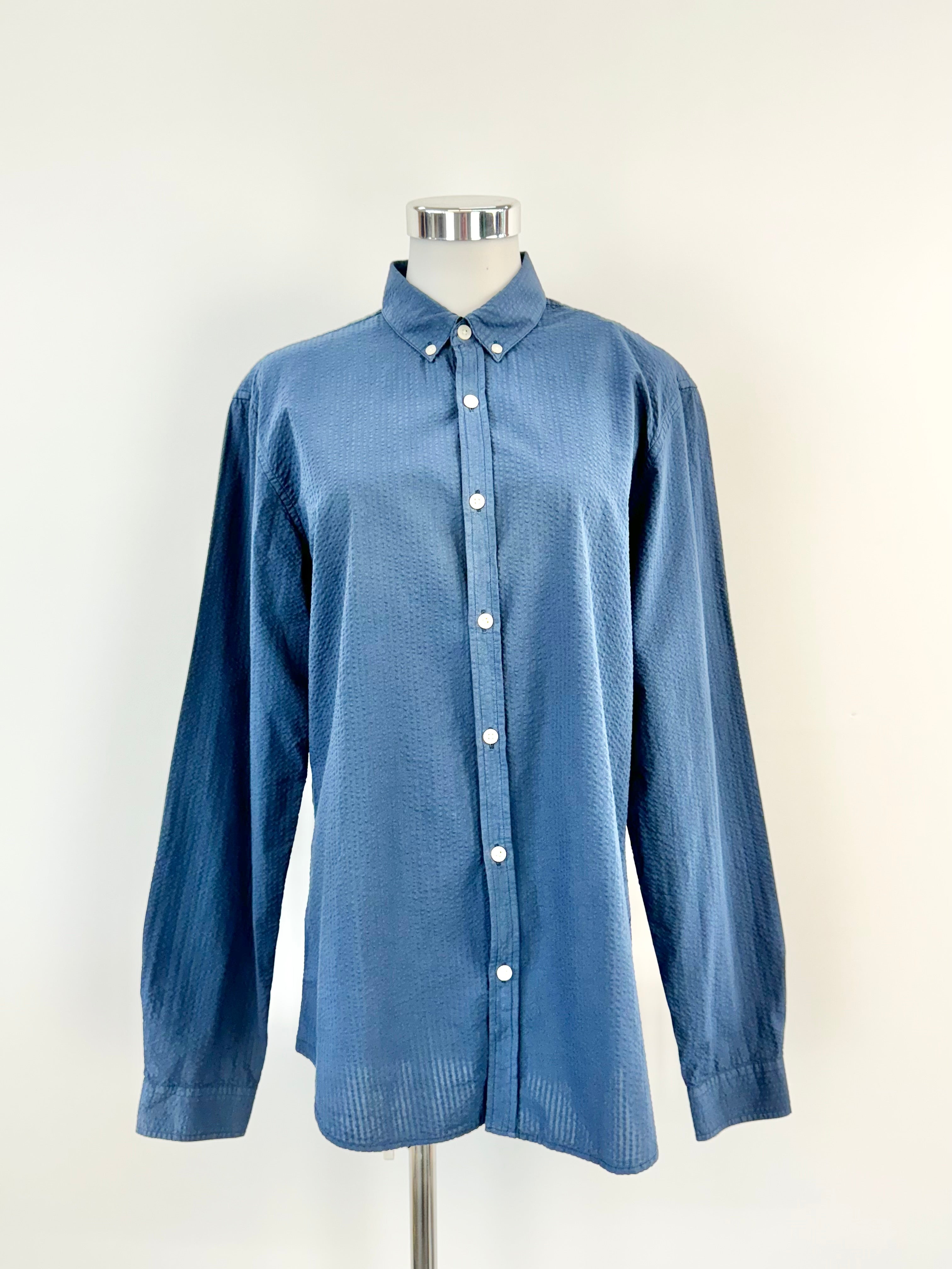 A blue shirt with small white buttons on a mannequin against a white background.