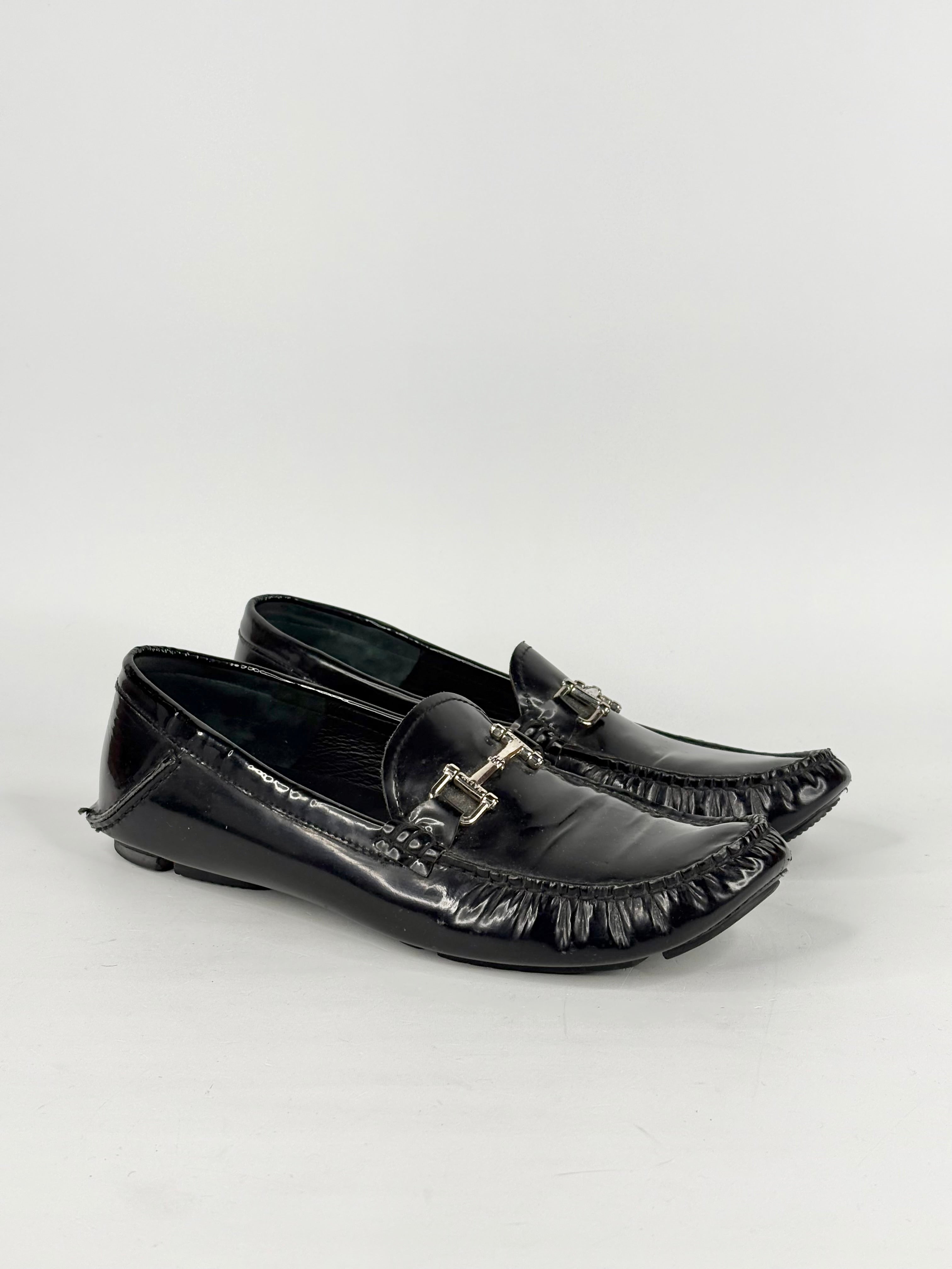 Black patent leather loafers with decorative buckles on a white background