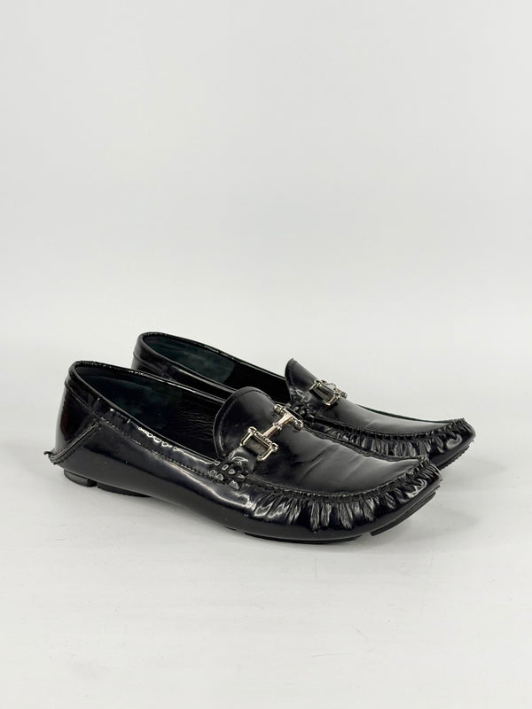 Black patent leather loafers with decorative buckles on a white background