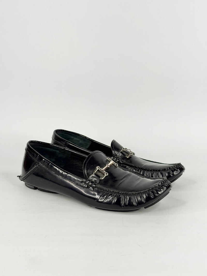 Black patent leather loafers with decorative buckles on a white background