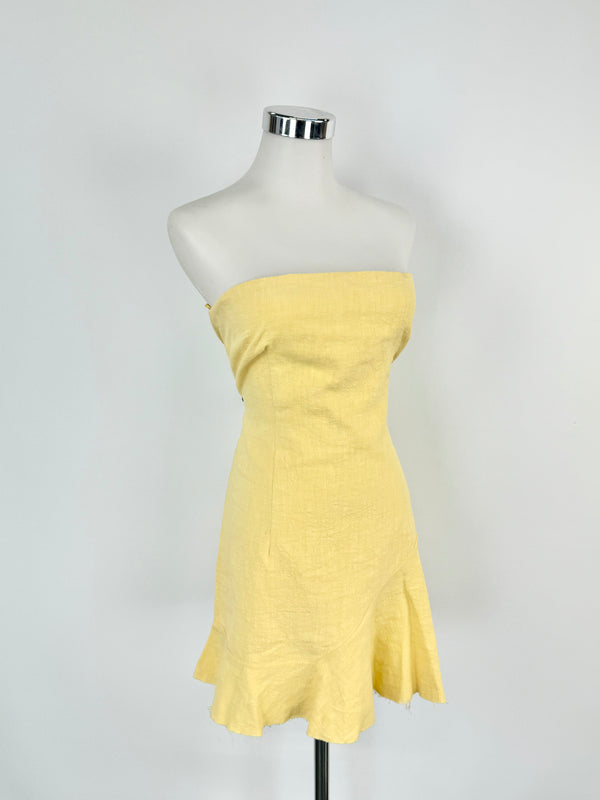 A light gold strapless dress on a mannequin, with boning around the bust and a slightly ruffled trim at the hem.