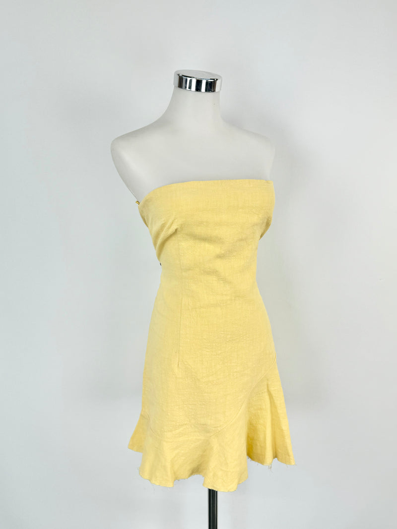 A light gold strapless dress on a mannequin, with boning around the bust and a slightly ruffled trim at the hem.