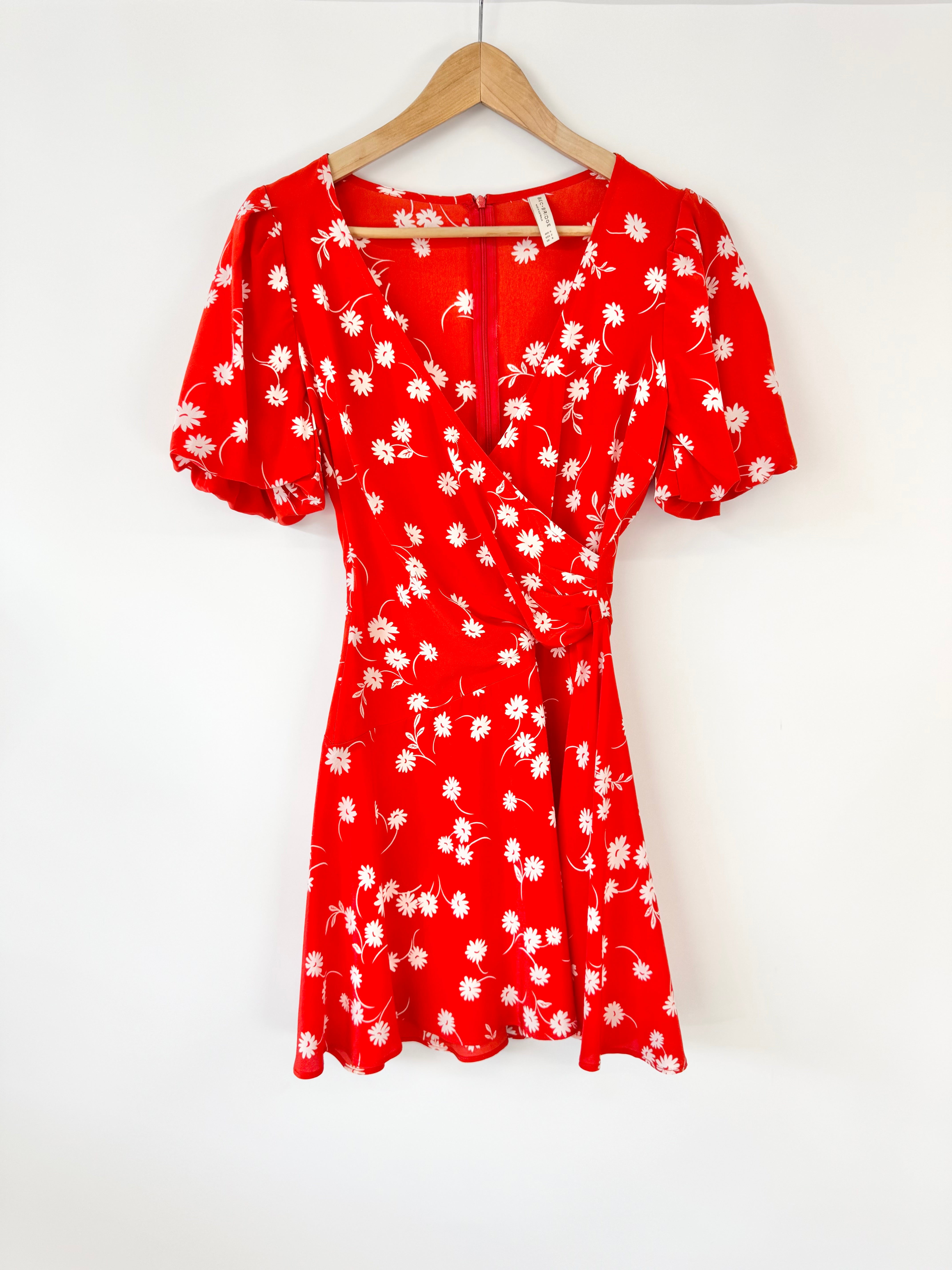 Red dress with white floral pattern on a hanger against a white background