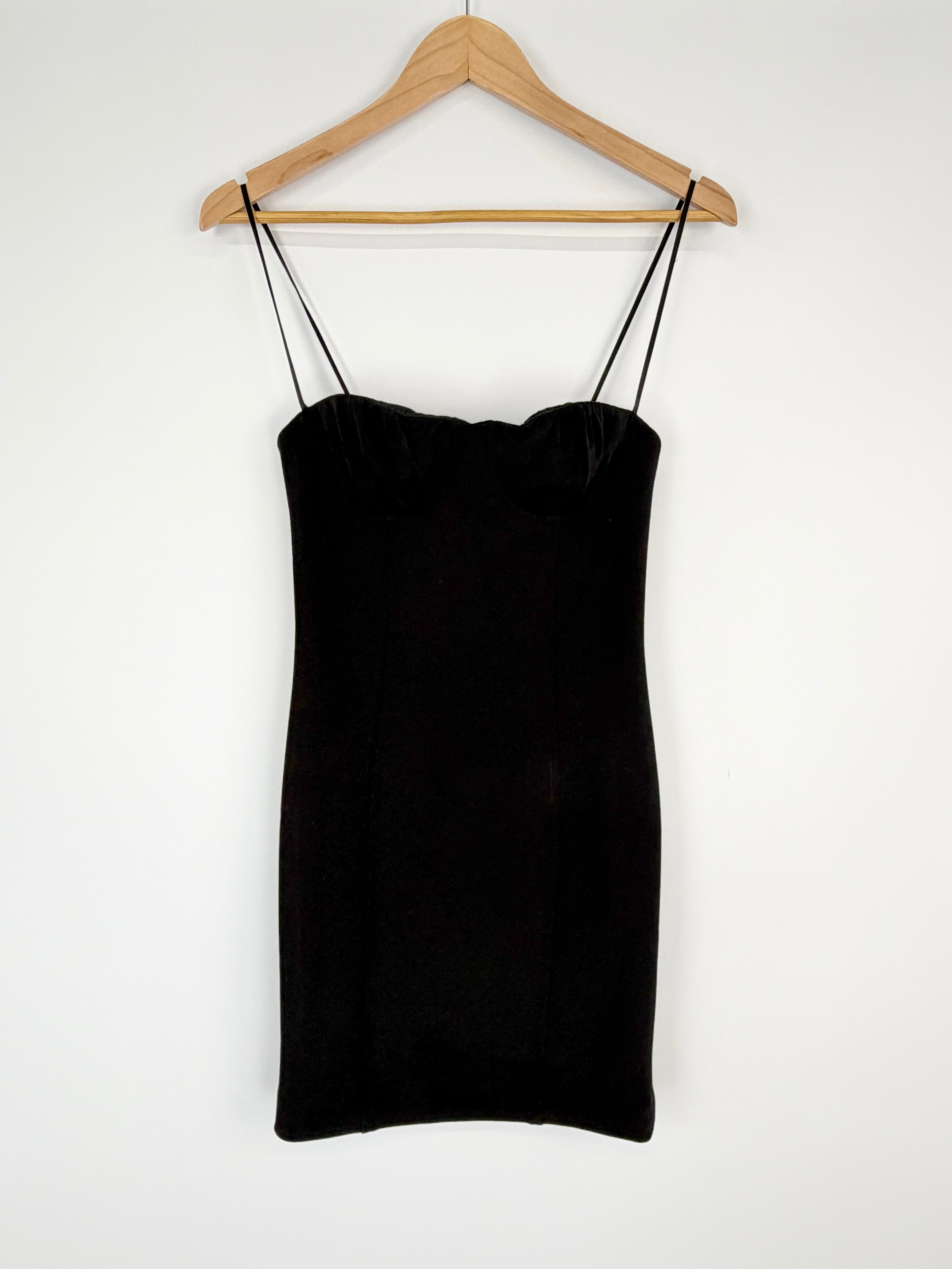 Black slip dress on a wooden hanger against a white background