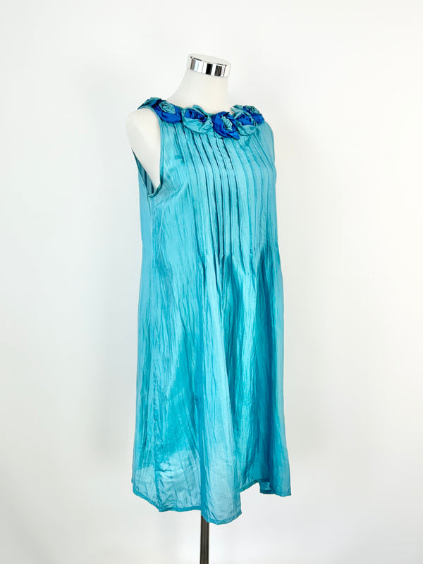 A blue silk dress with pintuck details and medium rosettes decorating the neckline, displayed on a mannequin.
