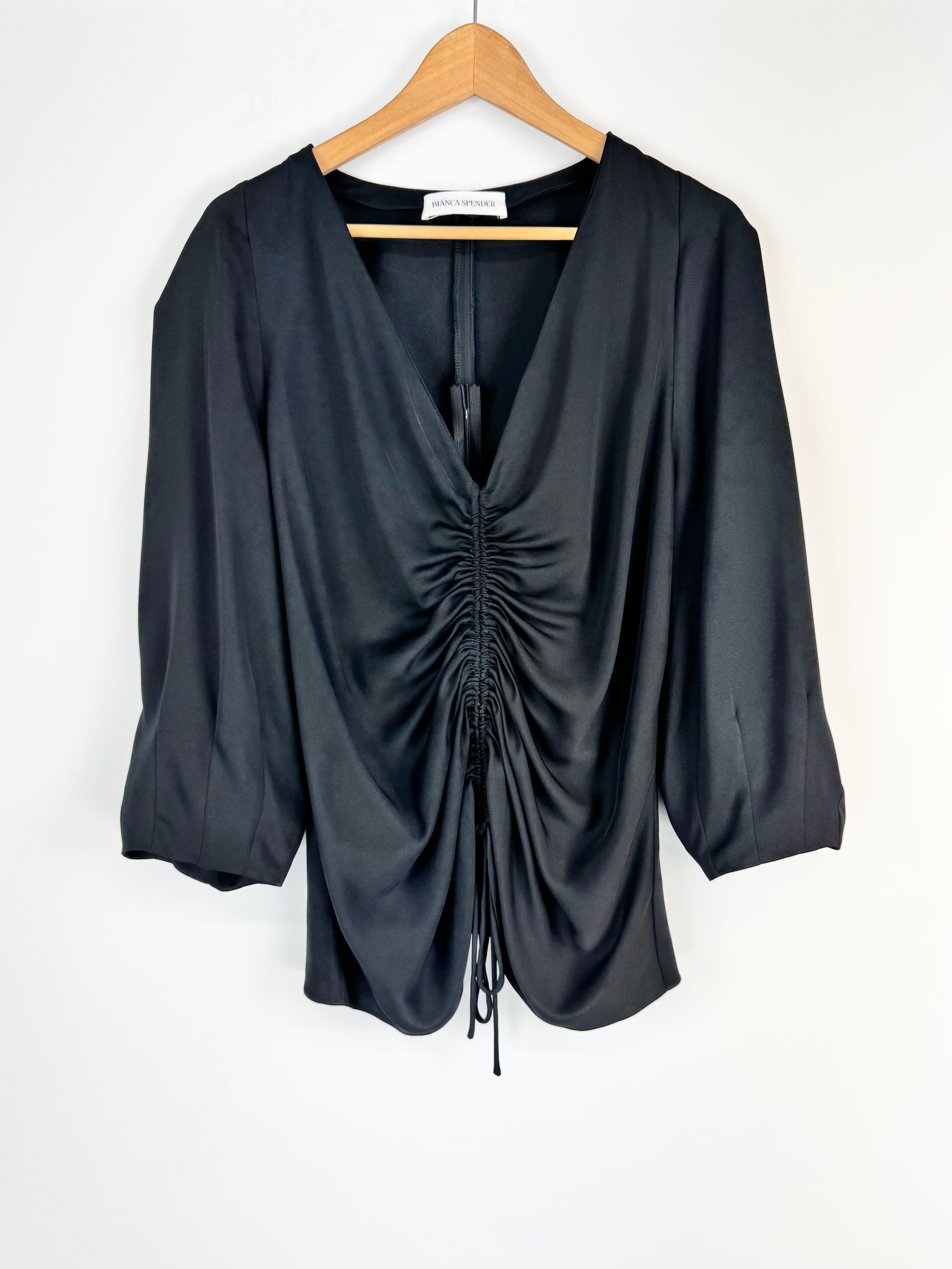 Black ruched blouse on a wooden hanger against a white background