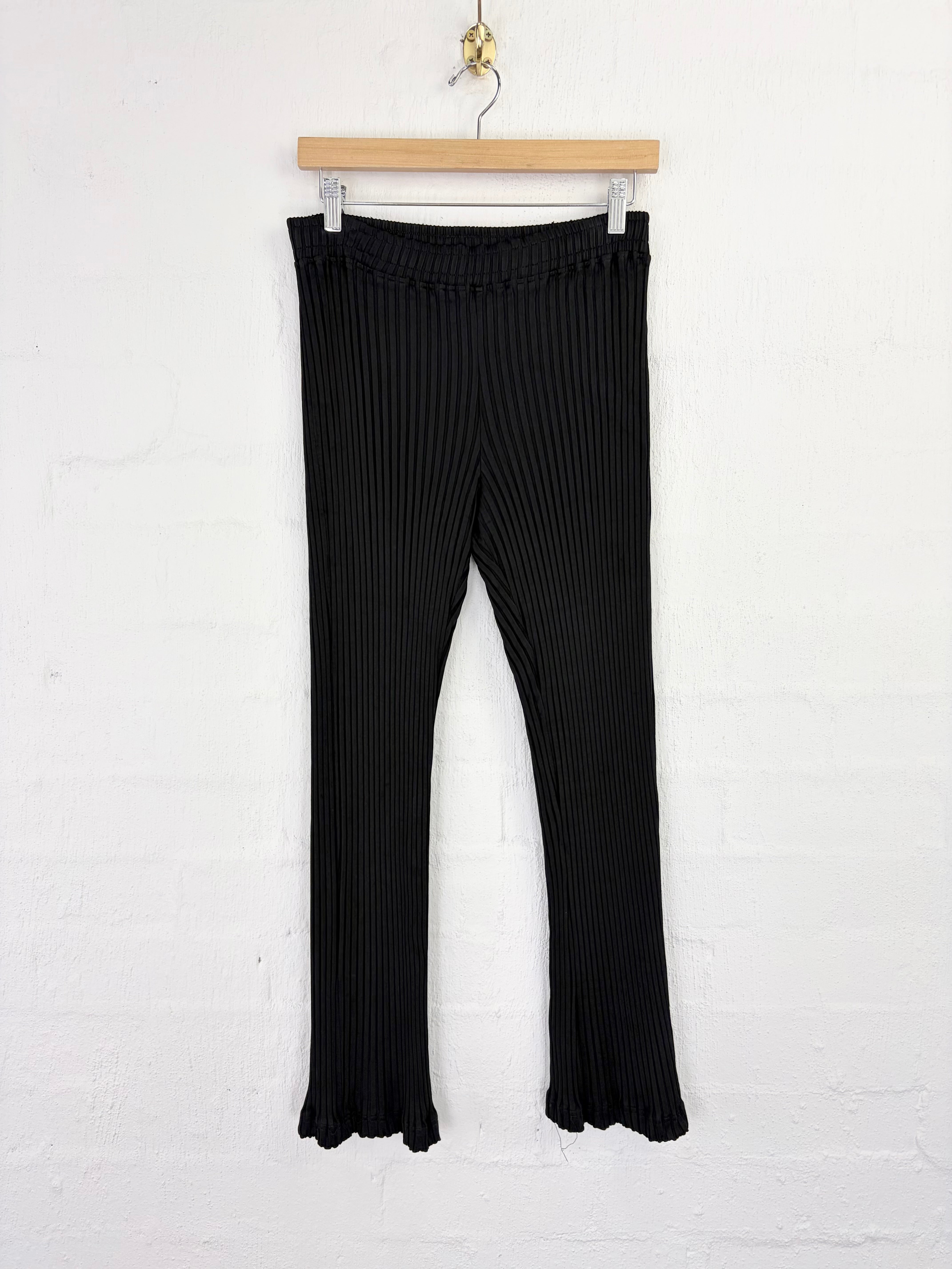 Black ribbed flare leggings hanging from a wooden hanger against a white brick wall.