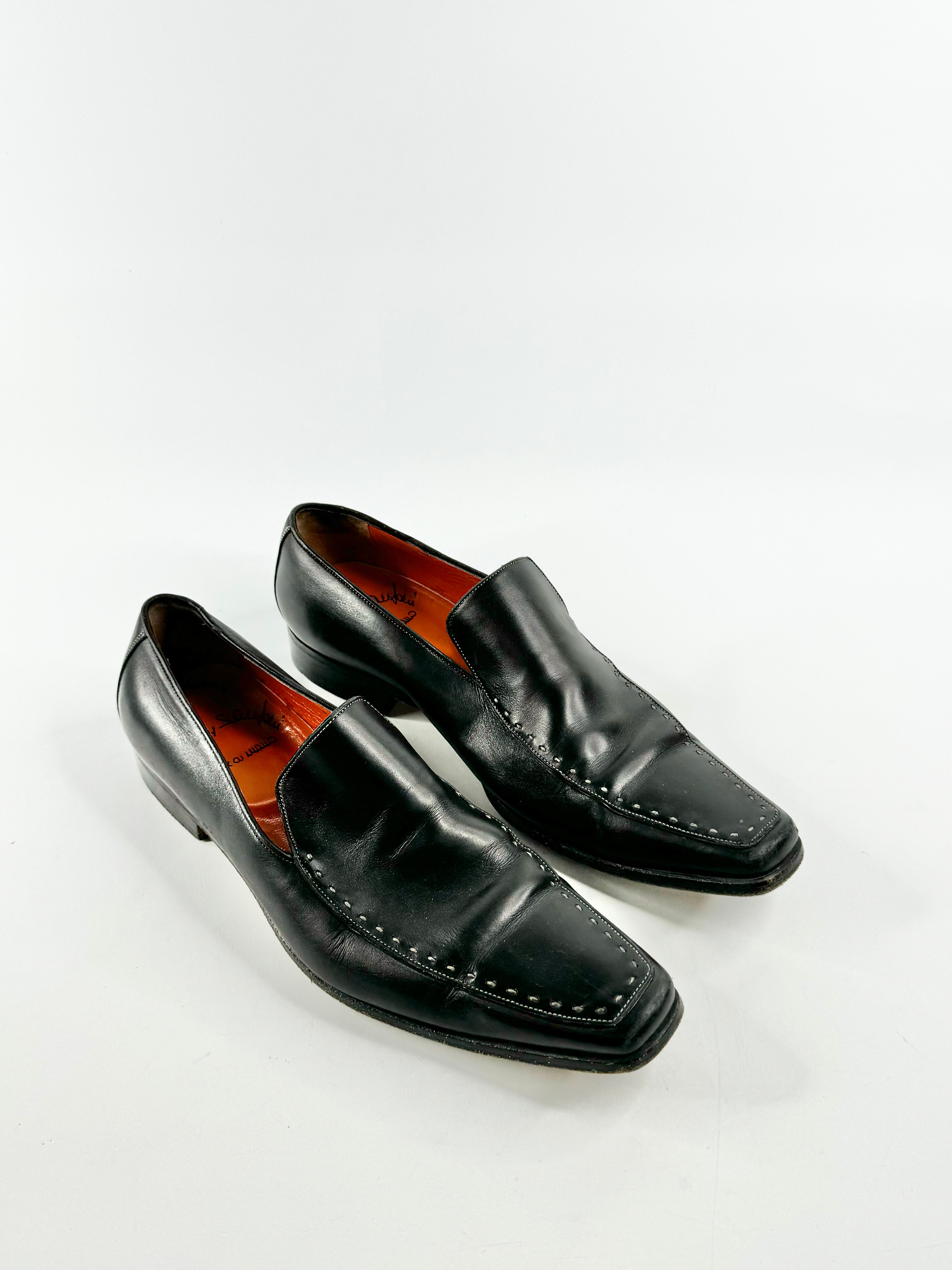 A pair of black elongated grey stitch loafers with visible wear on the tips and soles, displayed against a white background.