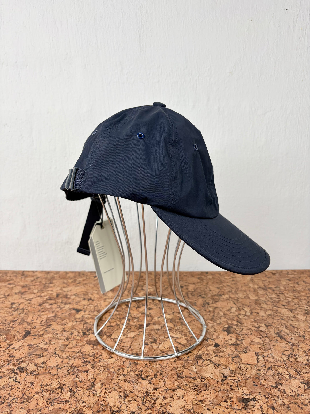 A dark navy blue baseball cap with a curved brim, displayed on a silver metal wire stand against a white wall and brown speckled countertop.