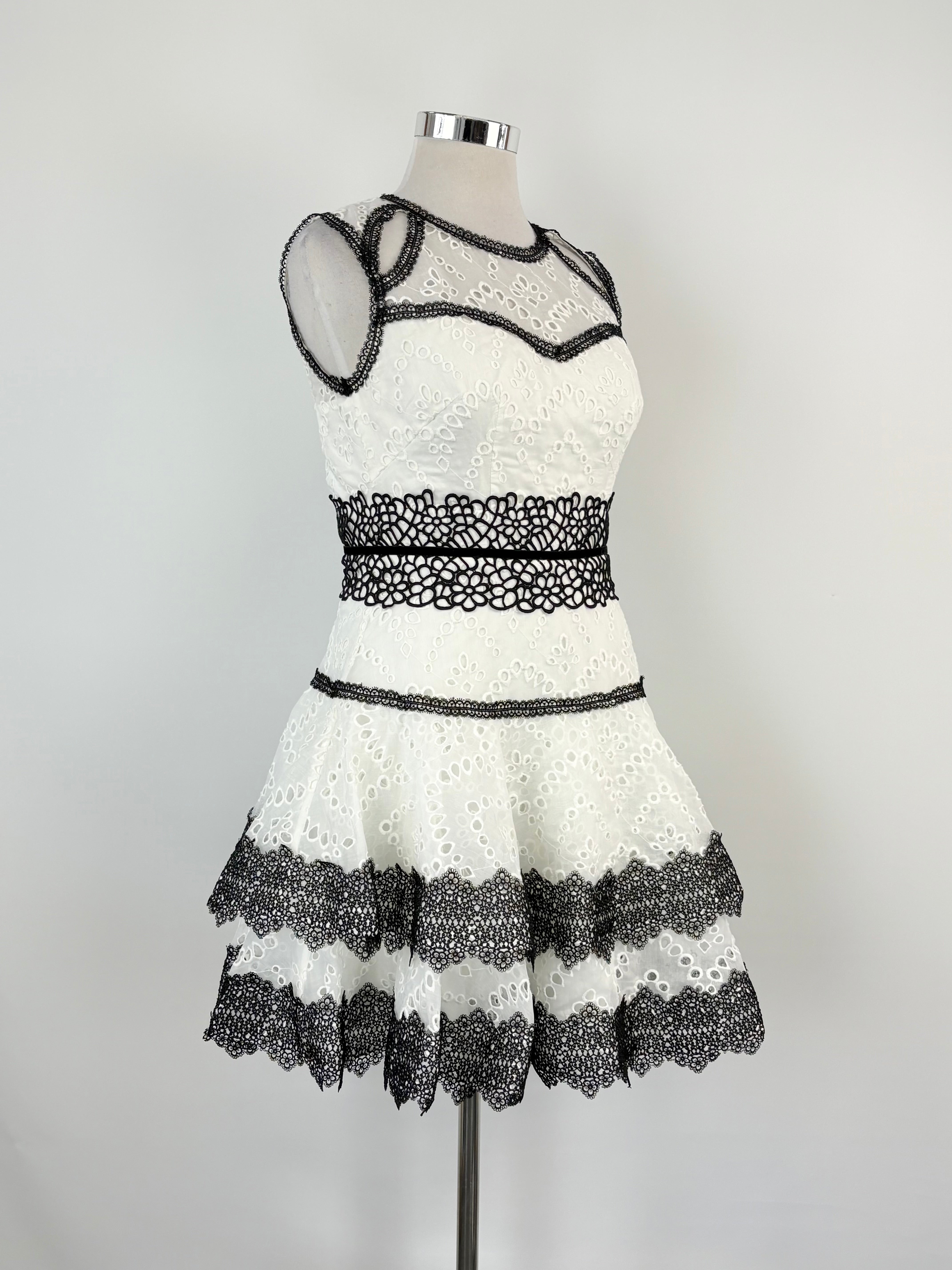A white mini dress with black trim and embroidered details, displayed on a mannequin against a plain background.