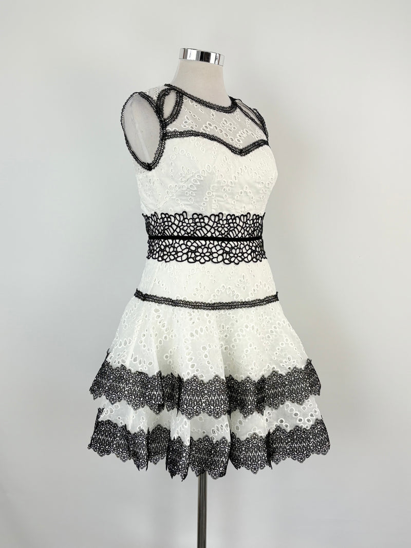 A white mini dress with black trim and embroidered details, displayed on a mannequin against a plain background.