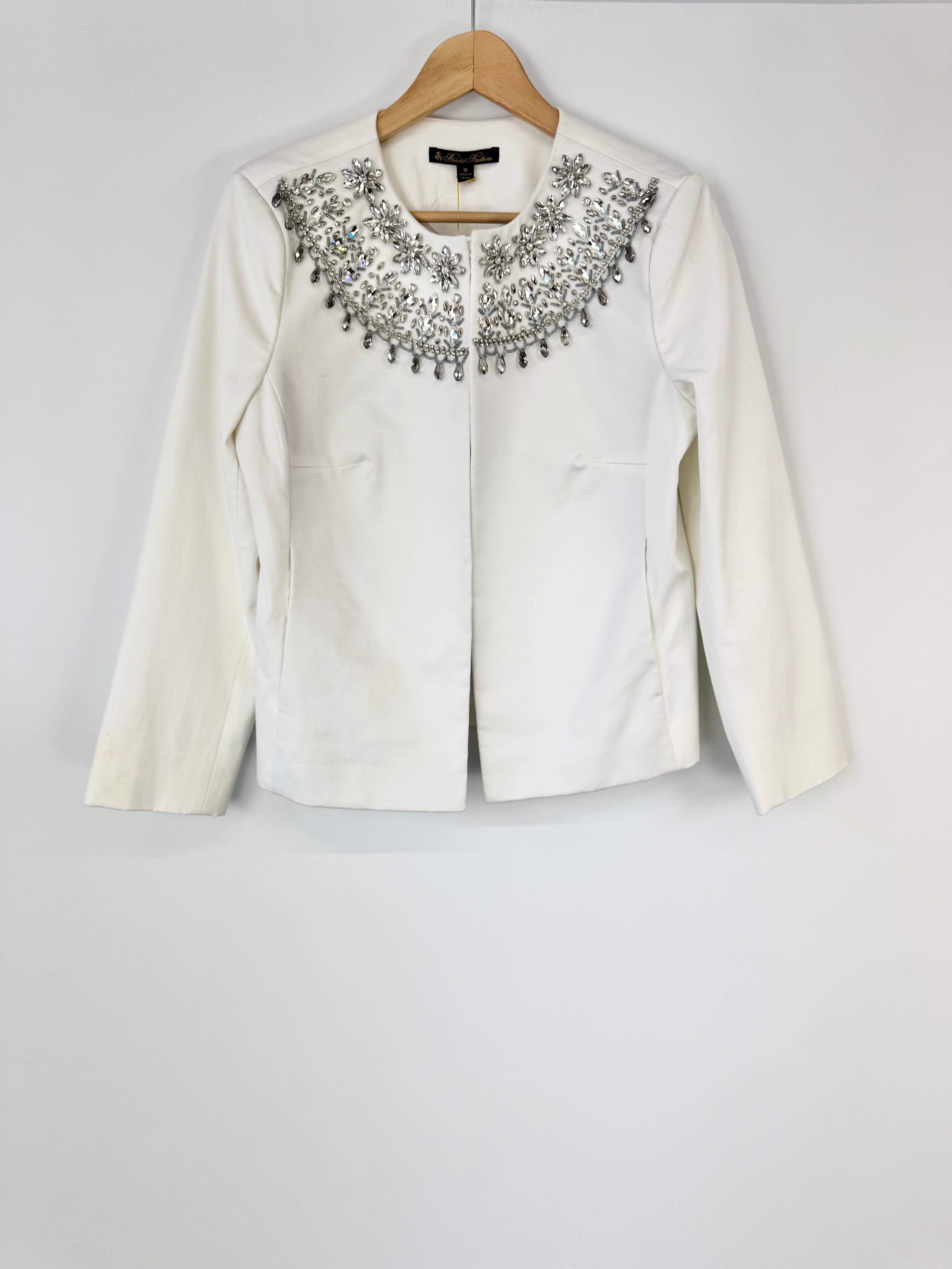 White jacket with decorative embellishments on a hanger against a white background