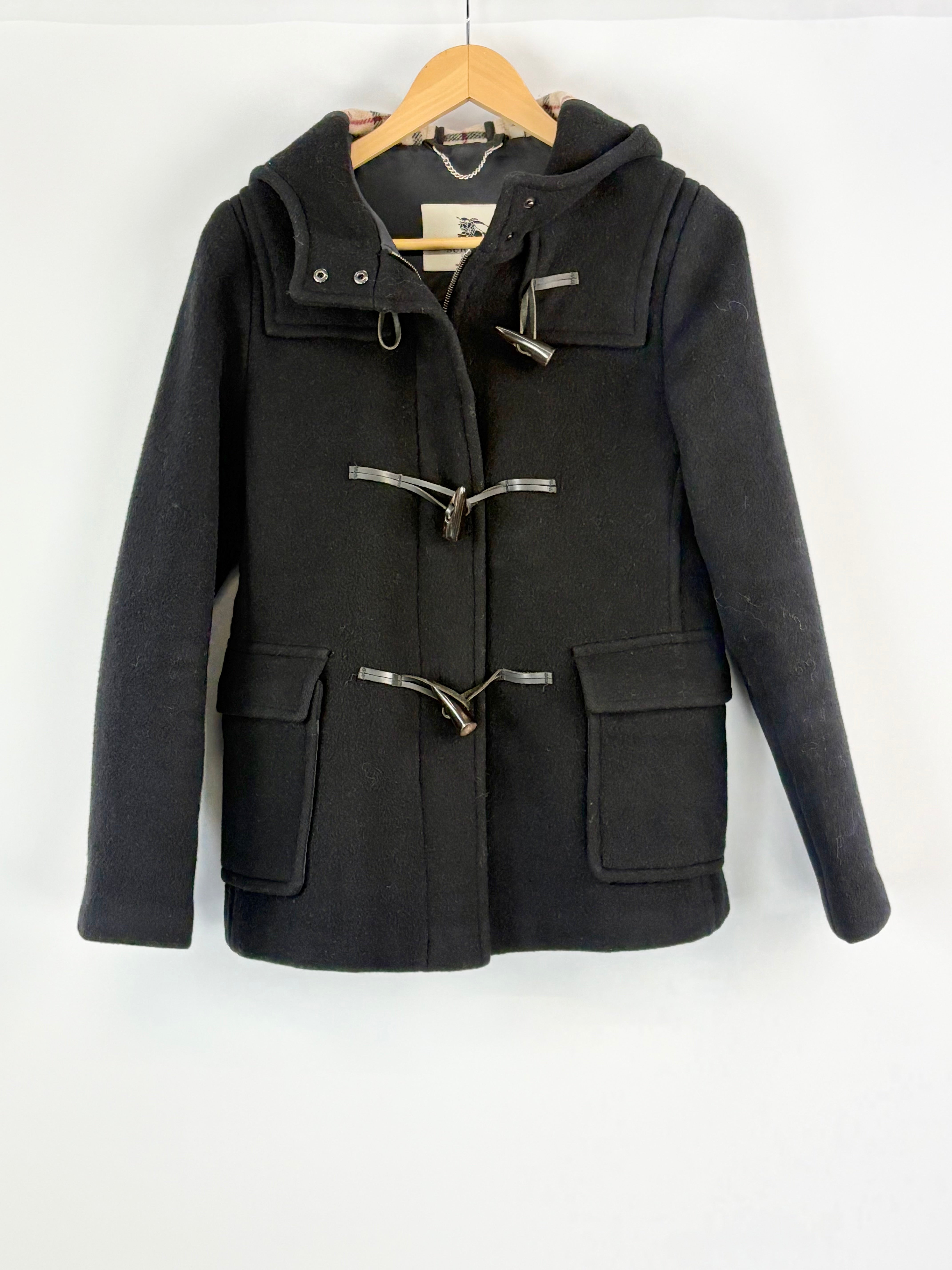 Black duffle coat on a hanger against a white background
