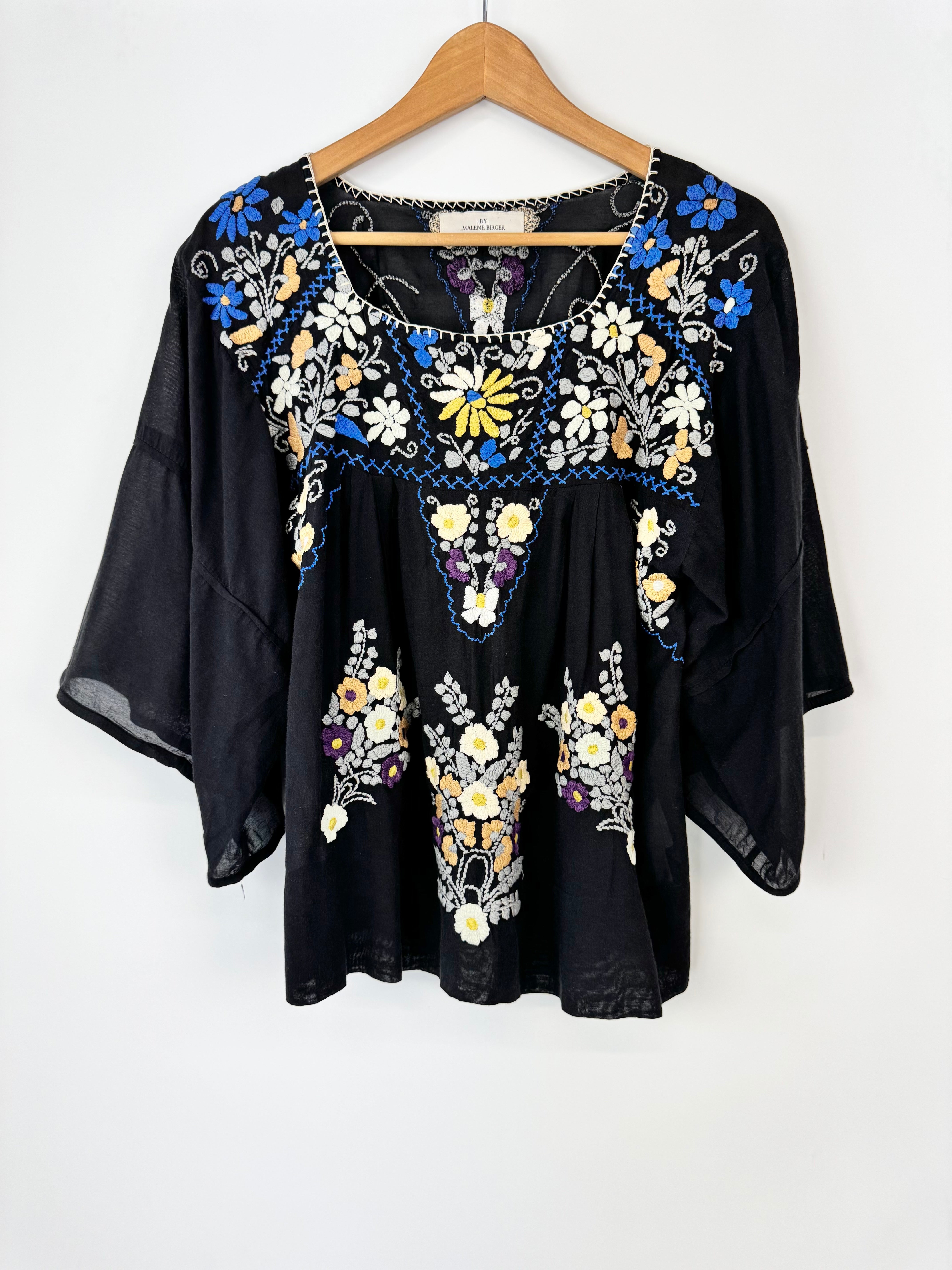 Black blouse with colorful floral embroidery on a hanger against a white background