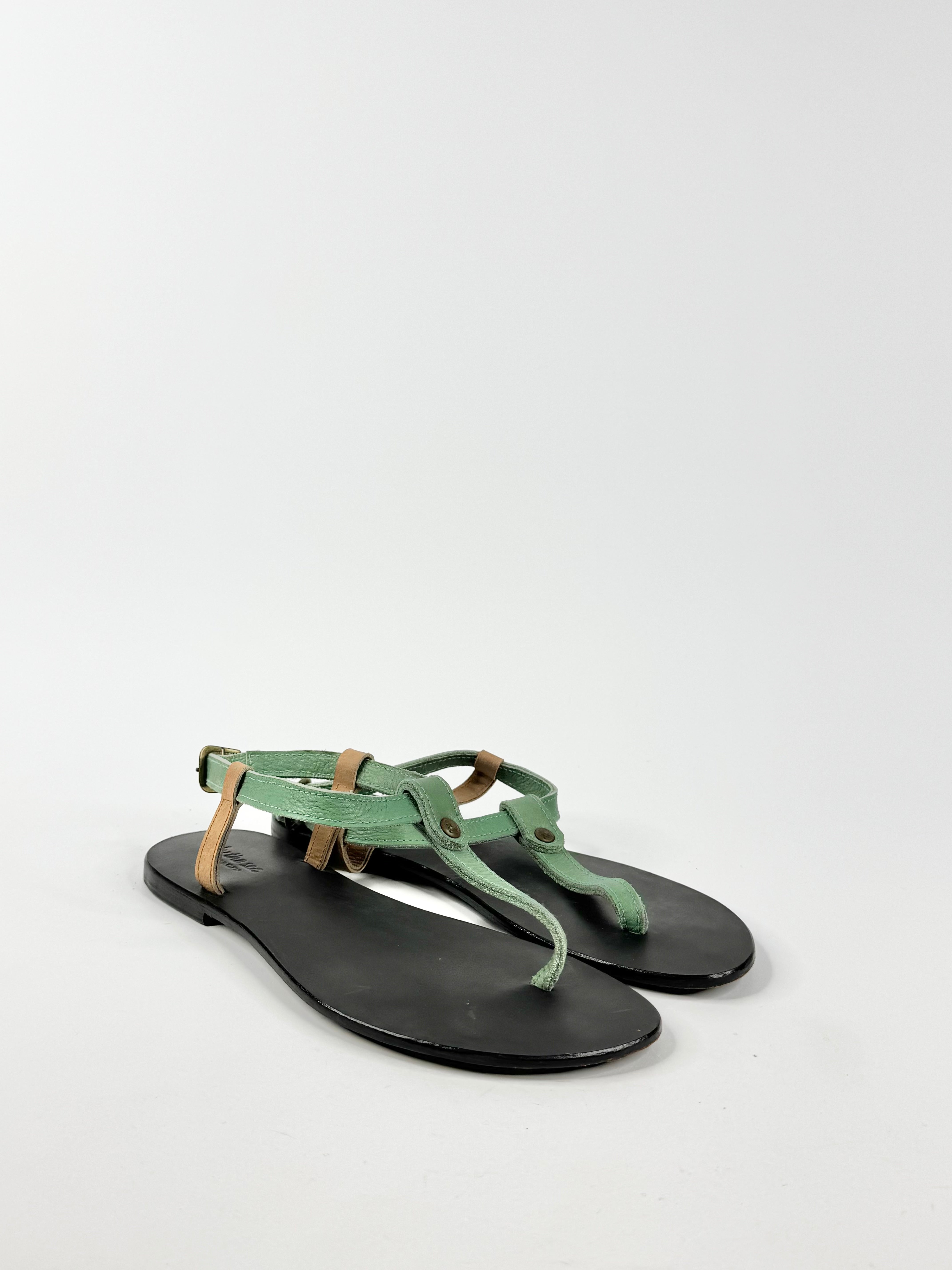Pair of green sandals with black soles on a light gray background