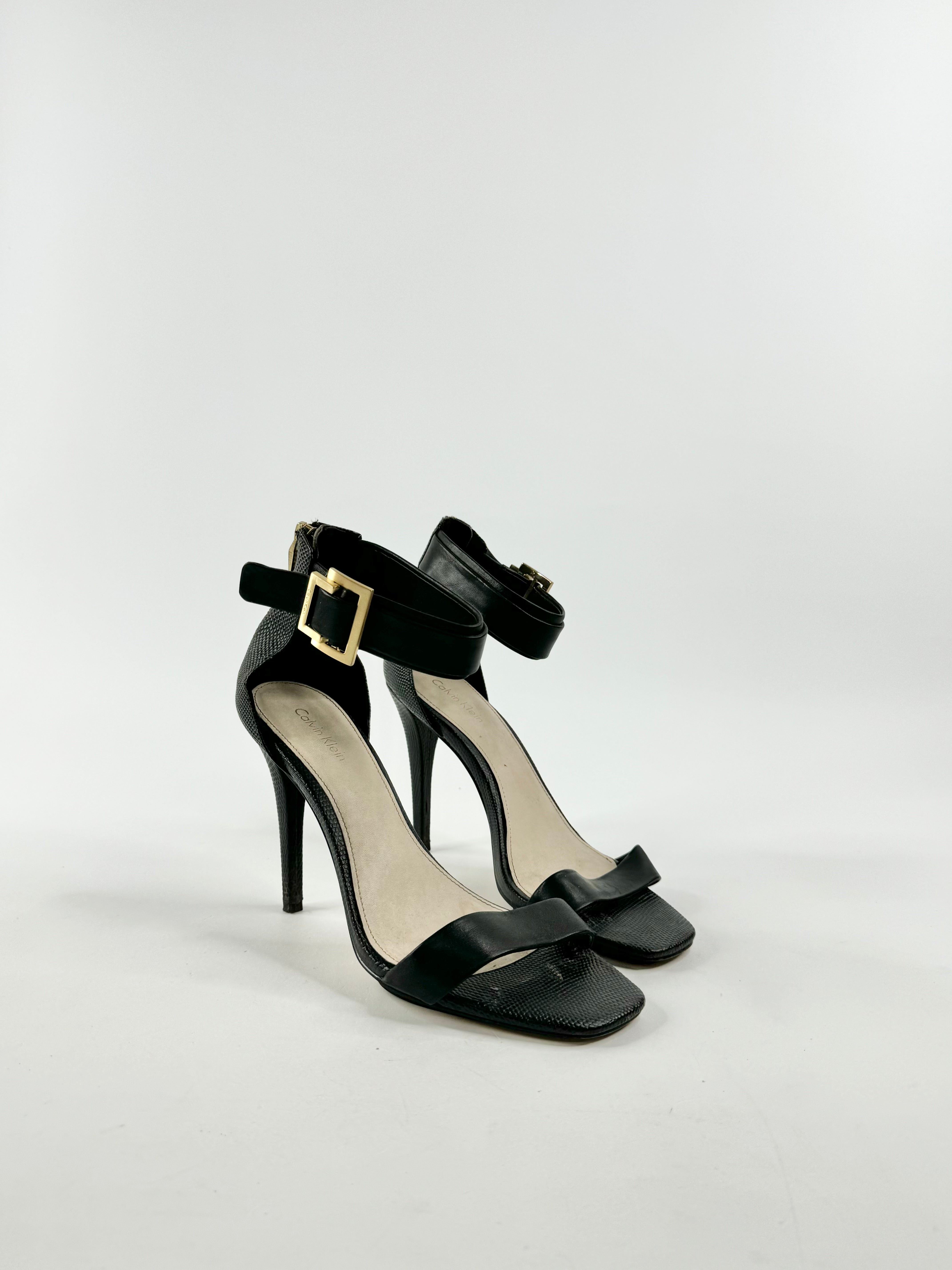 A pair of Calvin Klein black lizard texture stilettos with ankle straps and buckle details.