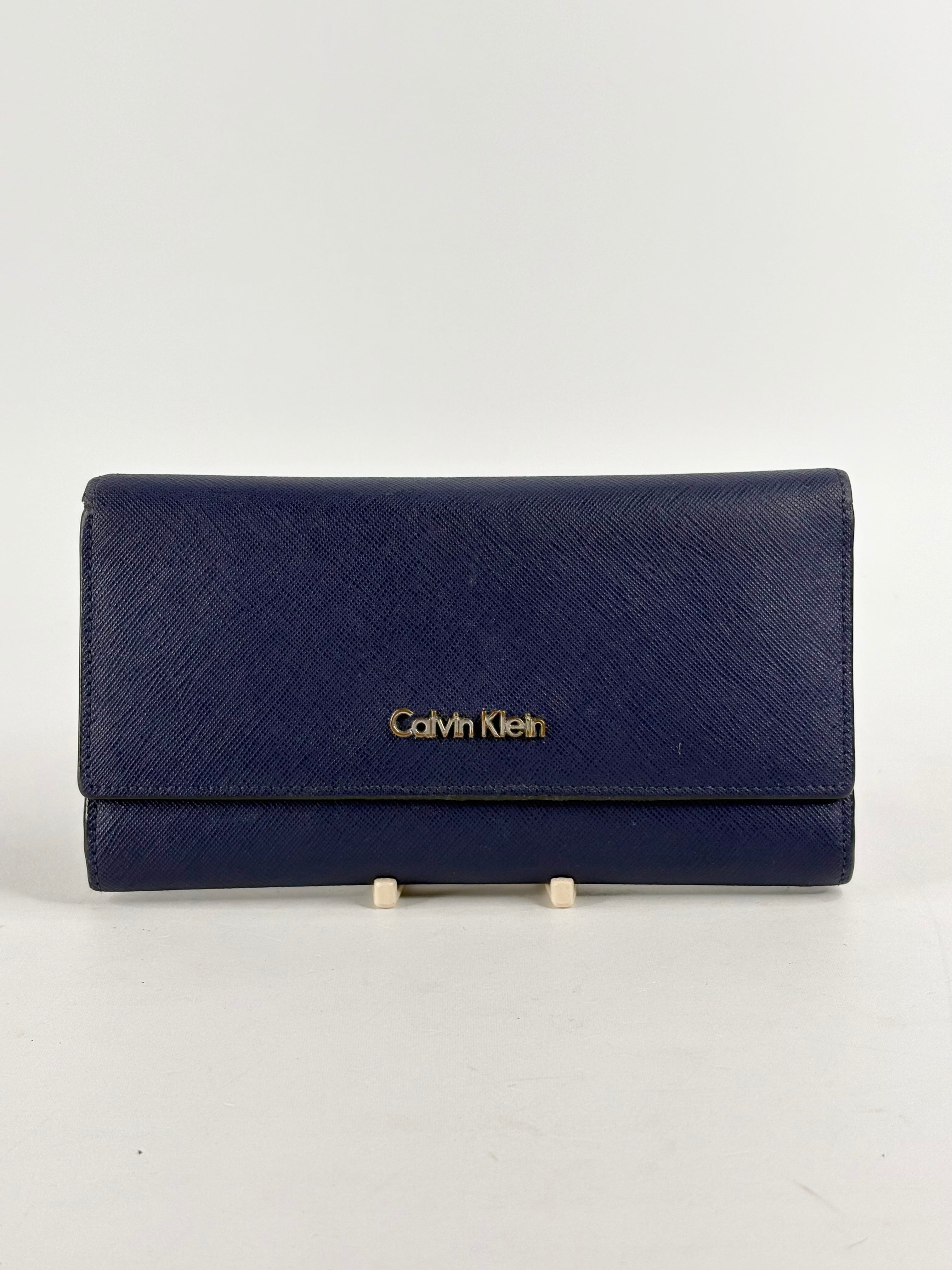 A Calvin Klein indigo leather trifold wallet displayed against a white background.