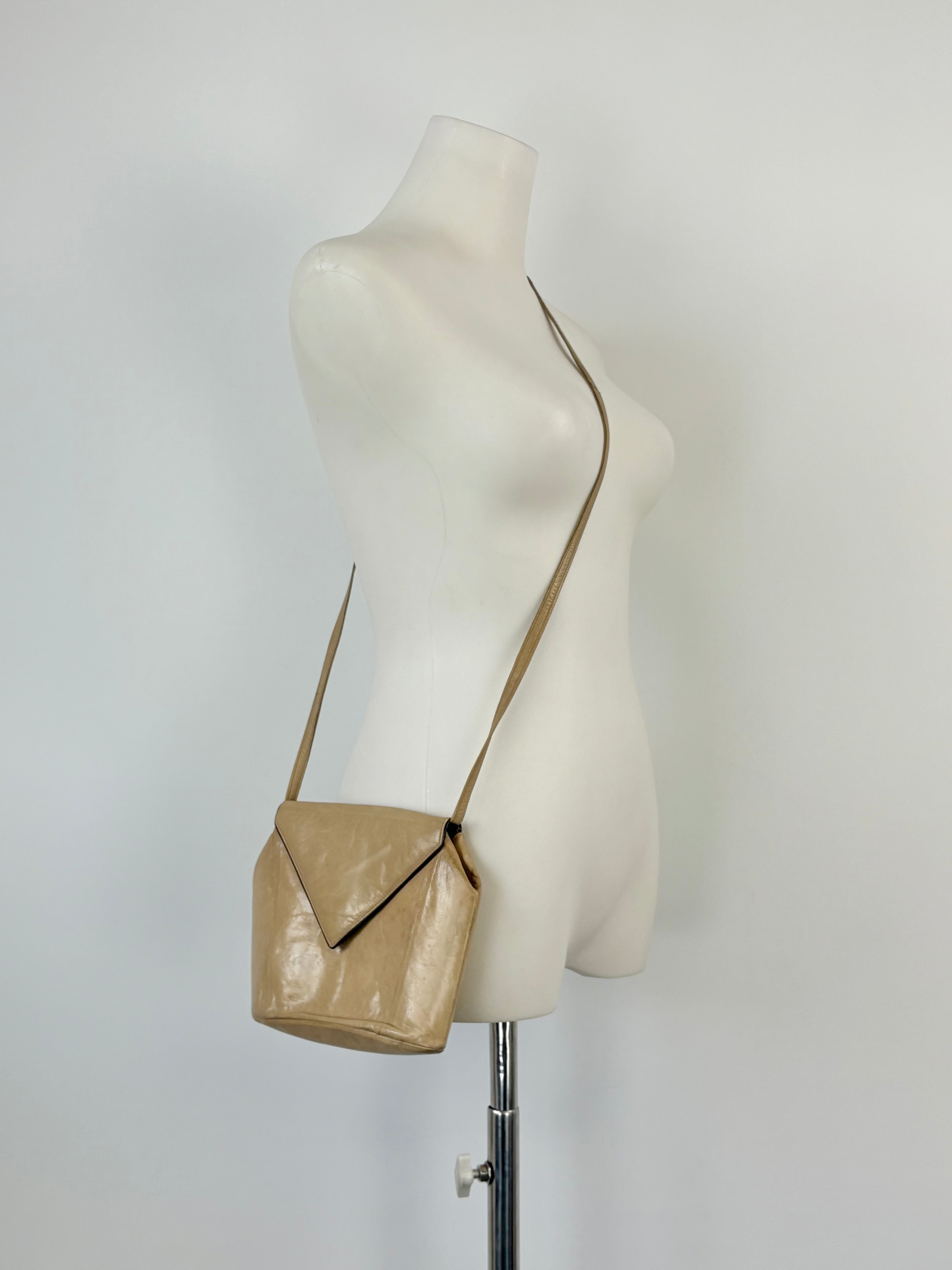 A beige leather mini envelope crossbody bag displayed on a mannequin.