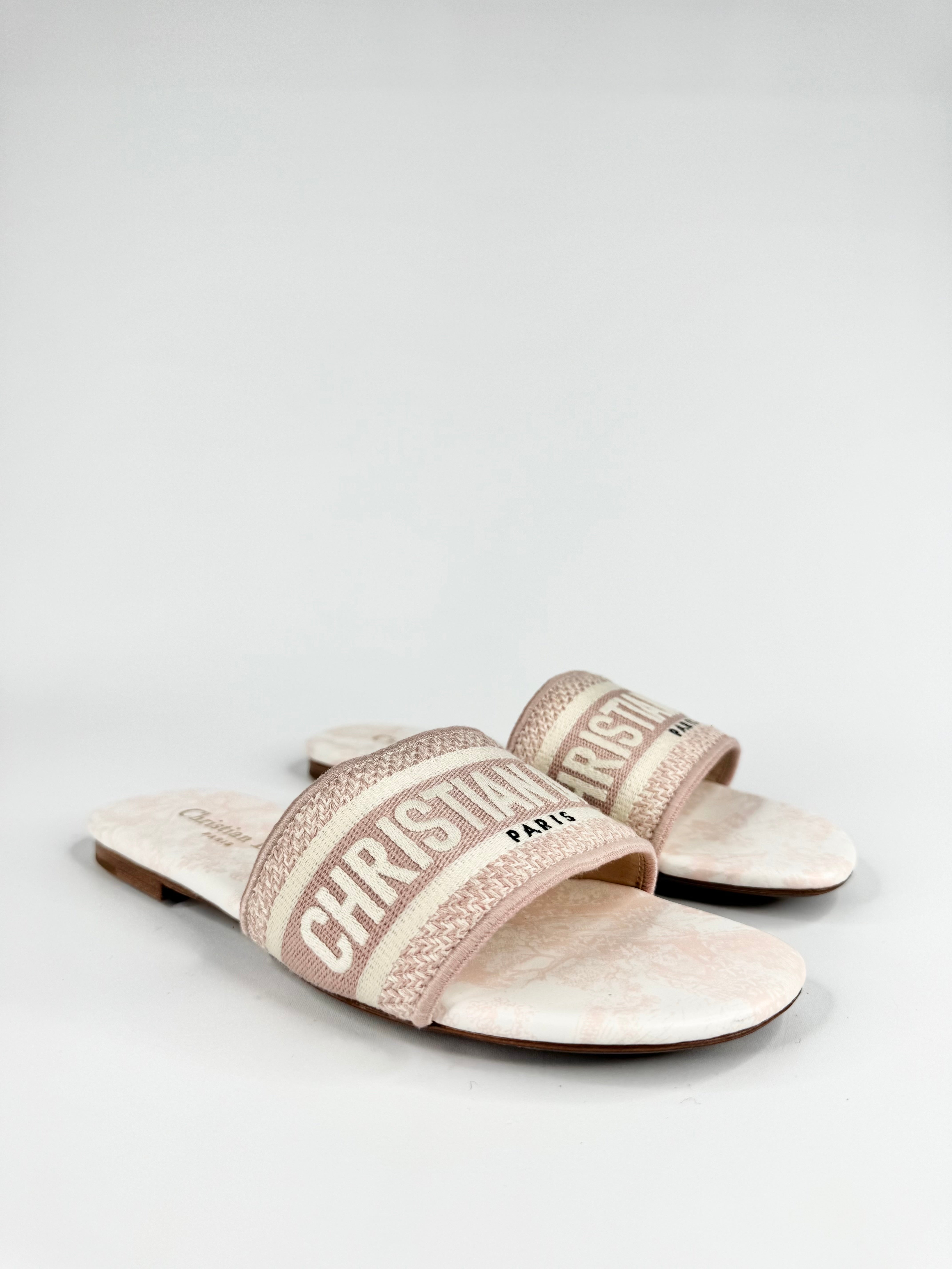 Pair of beige slides with 'Christian' branding on a white background
