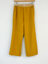 Mustard yellow pants on a hanger against a white background