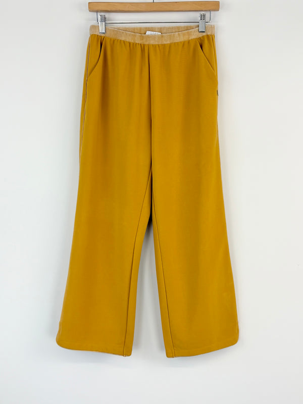 Mustard yellow pants on a hanger against a white background