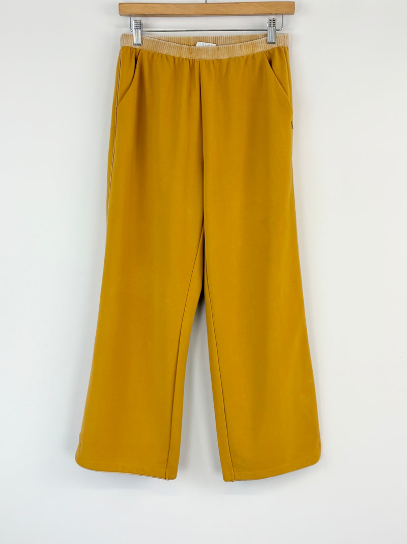 Mustard yellow pants on a hanger against a white background