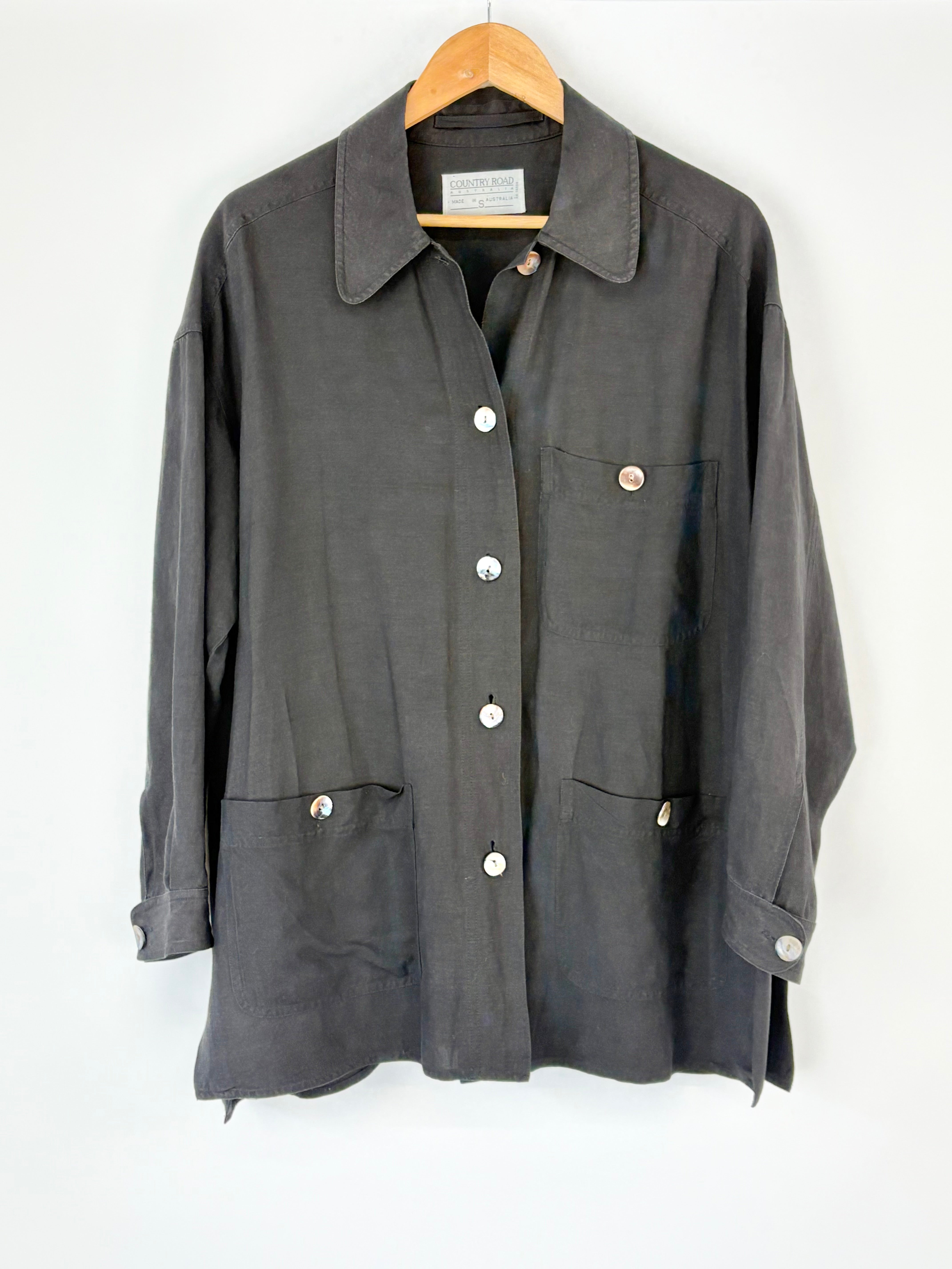 Black Country Road coat with button details on a wooden hanger against a white background