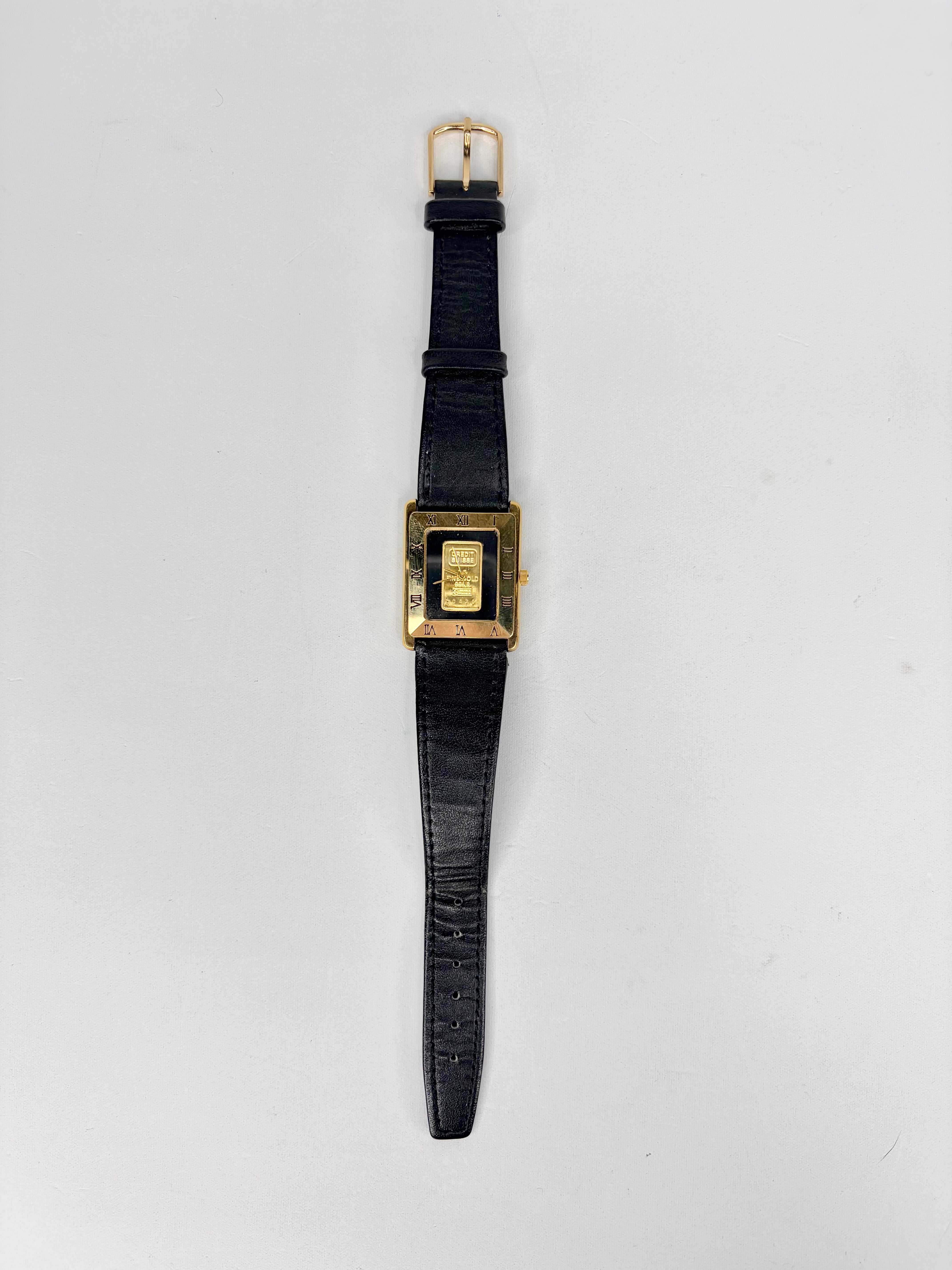 Watch with black strap and gold square face on a light gray background