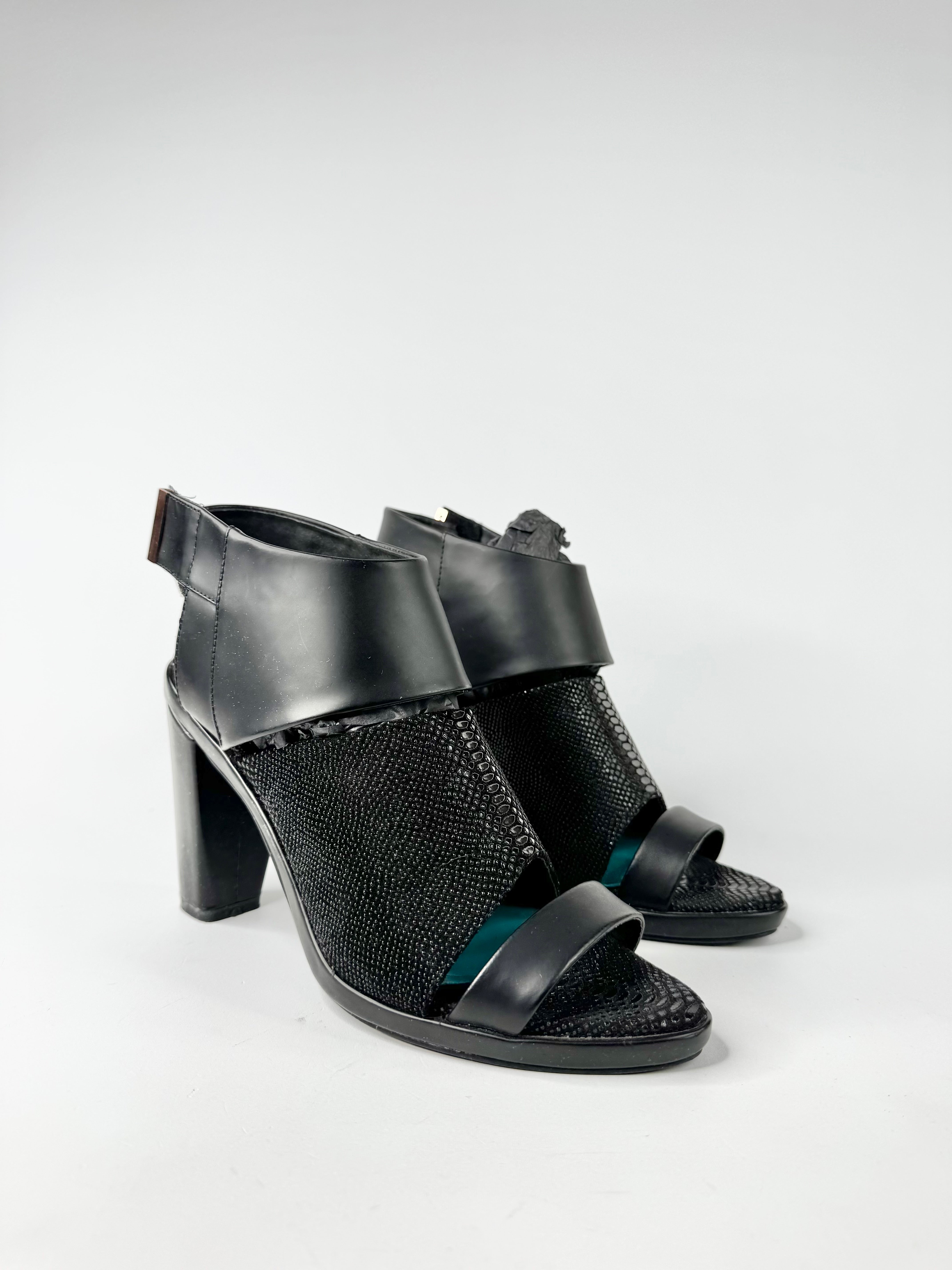 Black heeled sandals with reptile design on a white background