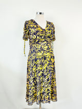 A yellow patterned ruched dress with short sleeves and a v-neckline on a mannequin, with the dress appearing to be knee to maxi length.