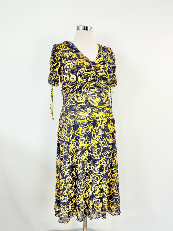 A yellow patterned ruched dress with short sleeves and a v-neckline on a mannequin, with the dress appearing to be knee to maxi length.