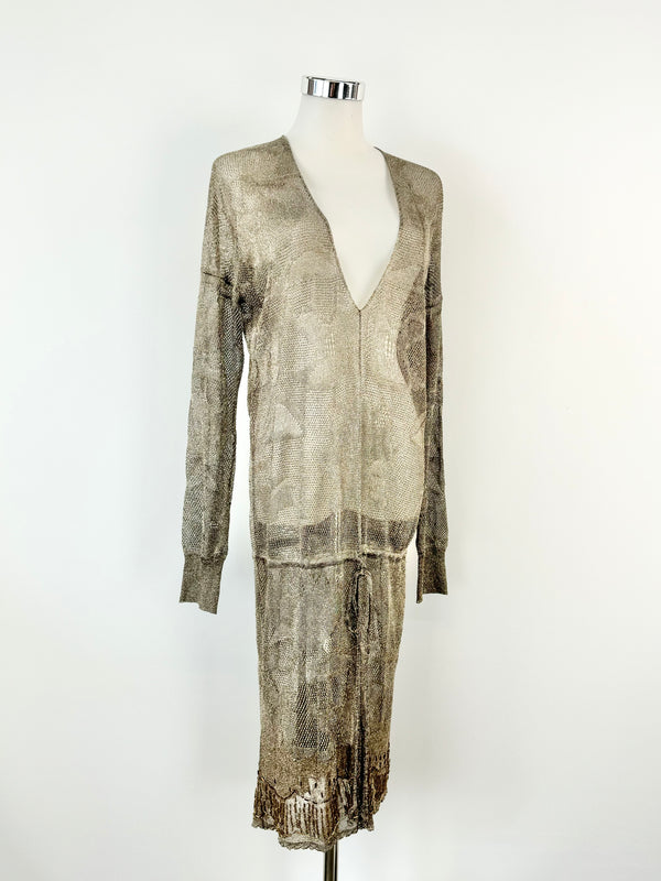 A metallic taupe sheer knit dress with a long v-neckline, long sleeves, and drawstring below the waist, displayed on a mannequin.