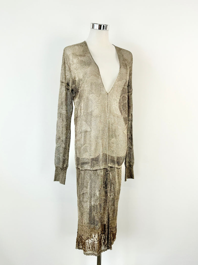 A metallic taupe sheer knit dress with a long v-neckline, long sleeves, and drawstring below the waist, displayed on a mannequin.