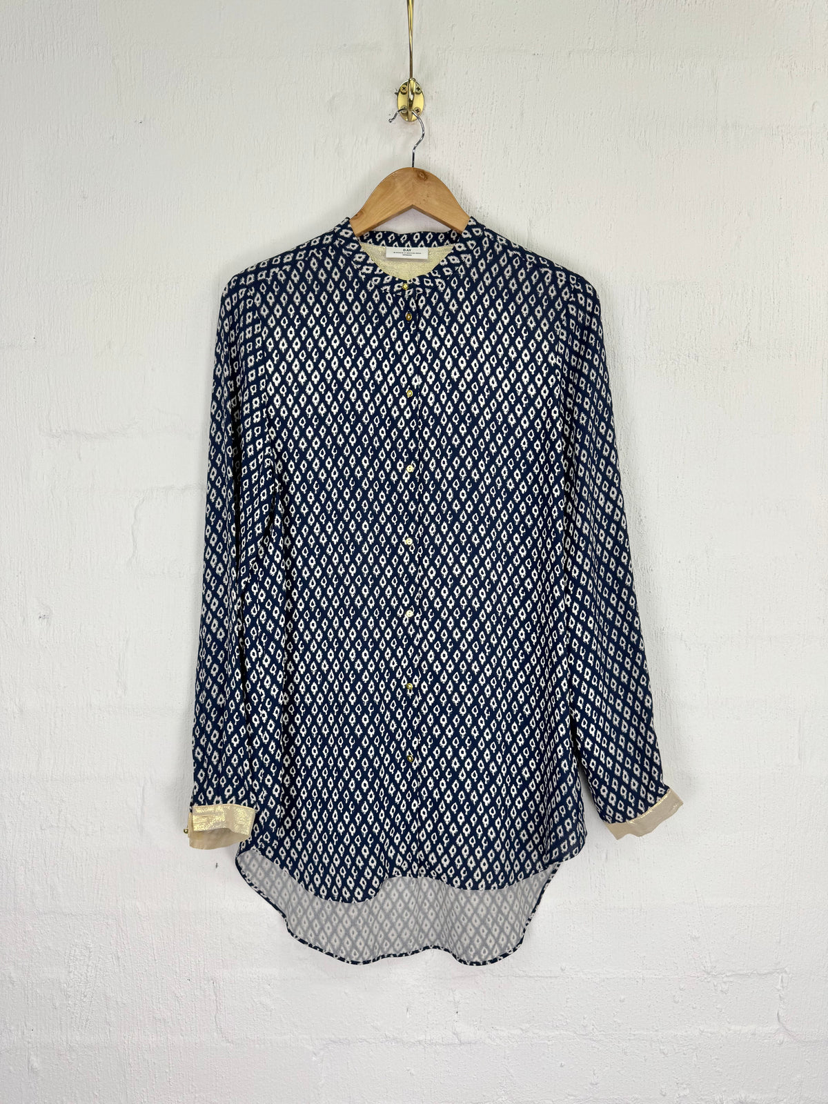 A navy blue and white geometric patterned long-sleeve blouse hanging on a wooden hanger against a white brick wall.