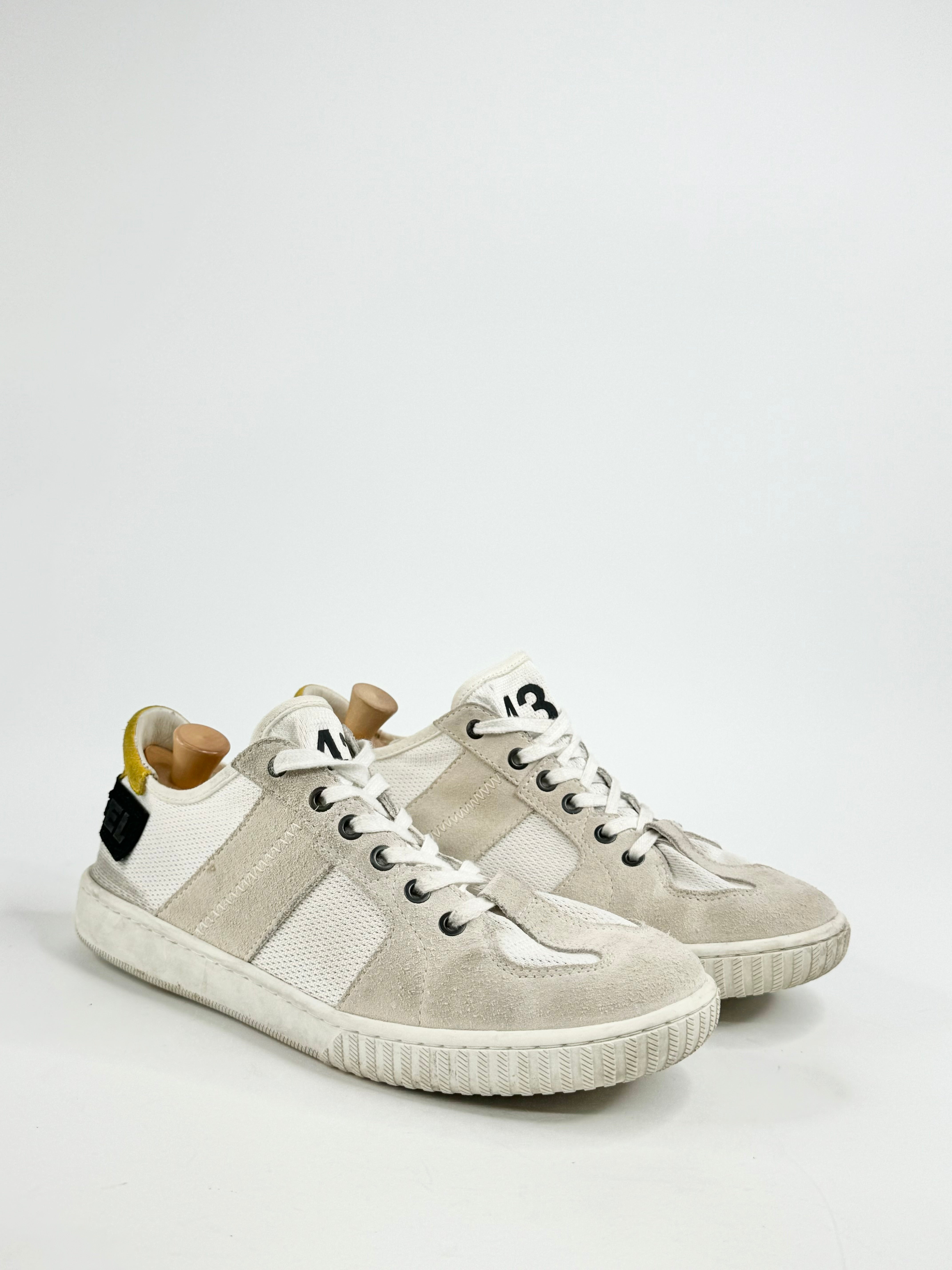 A pair of white mesh sneakers with gray suede accents and a yellow suede patch on the heel, featuring a rubber sole.