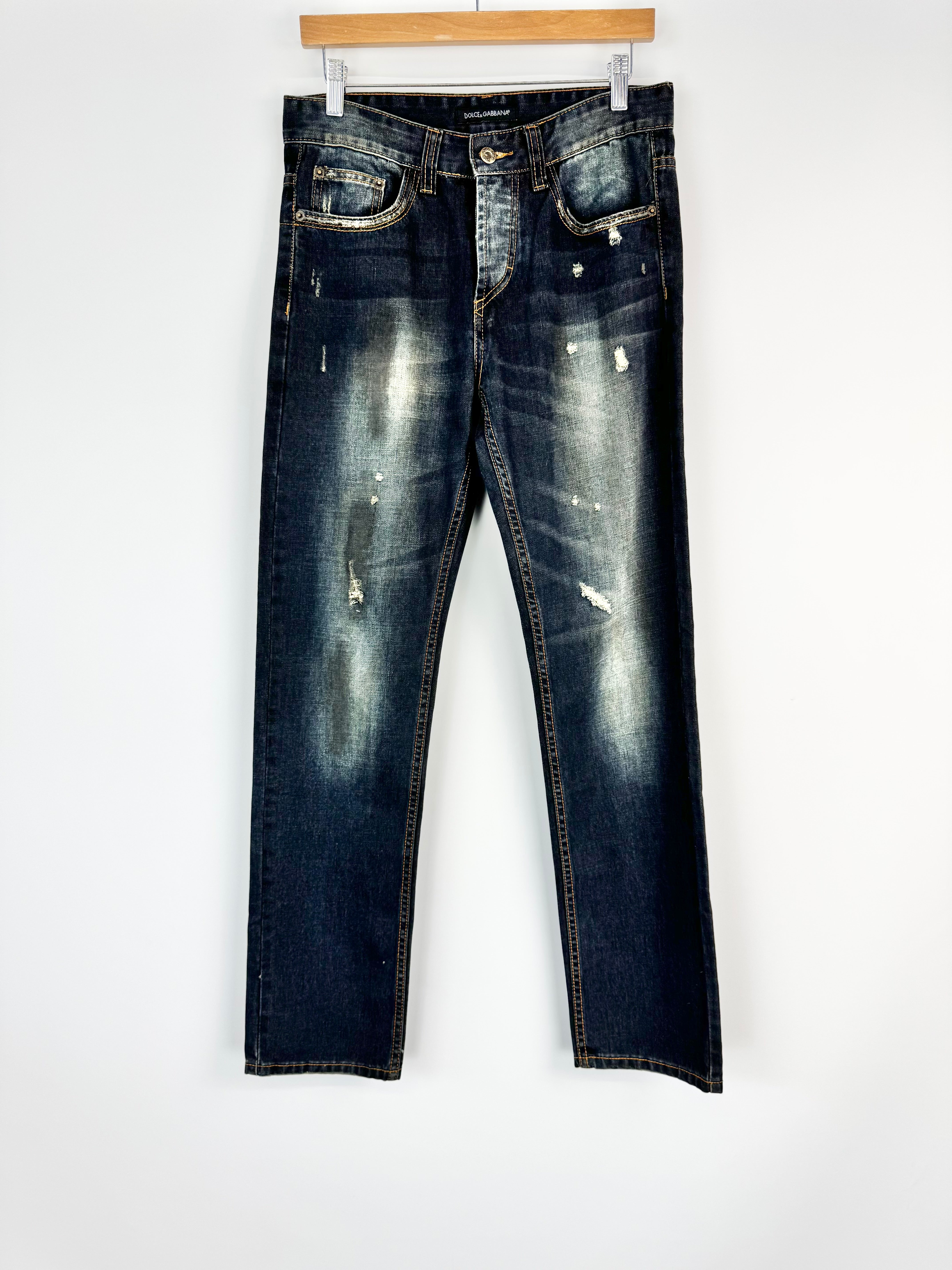 Pair of distressed blue jeans hanging on a wooden hanger against a white background