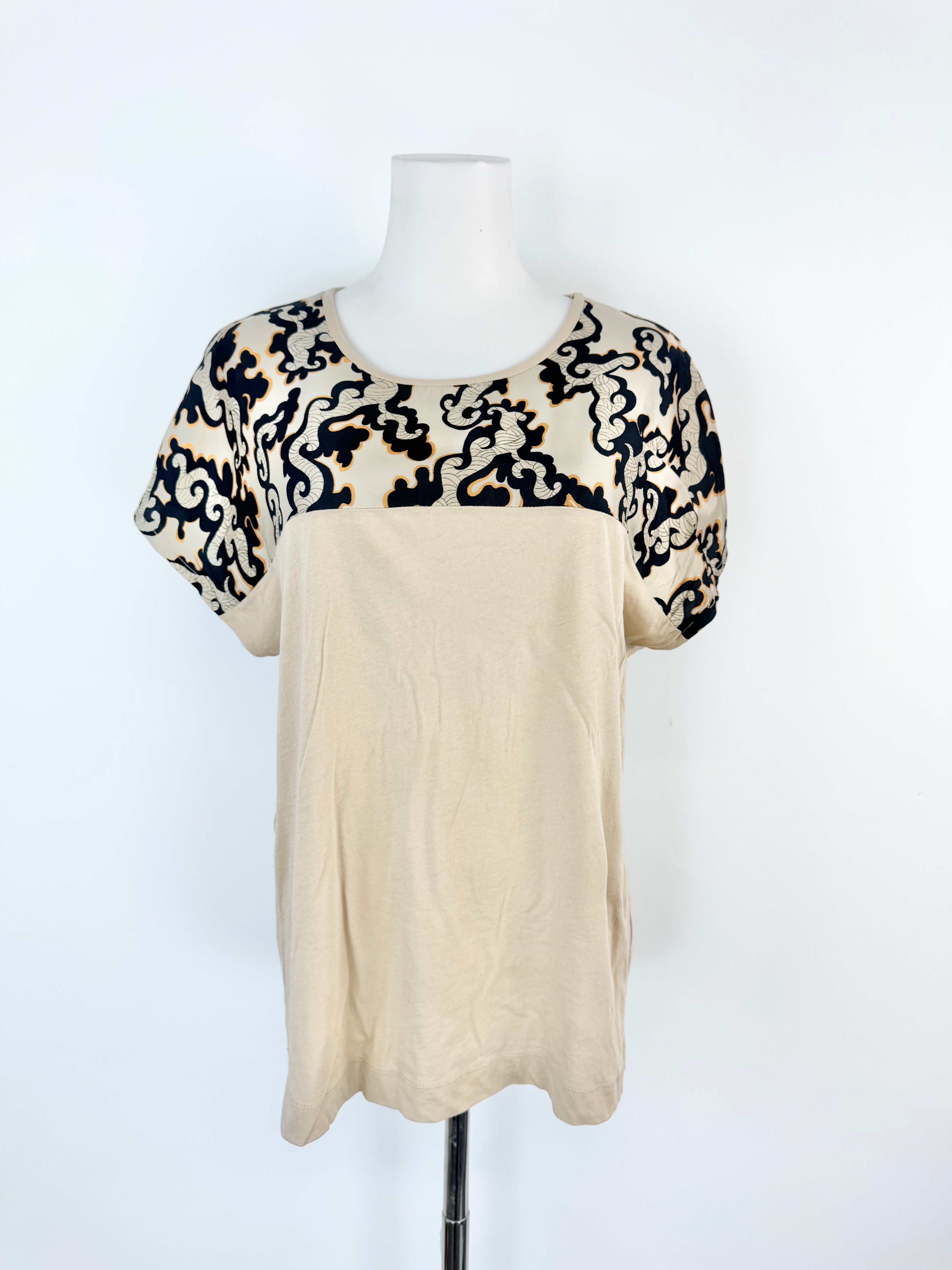 Mannequin wearing a beige top with black and white patterned sleeves on a white background
