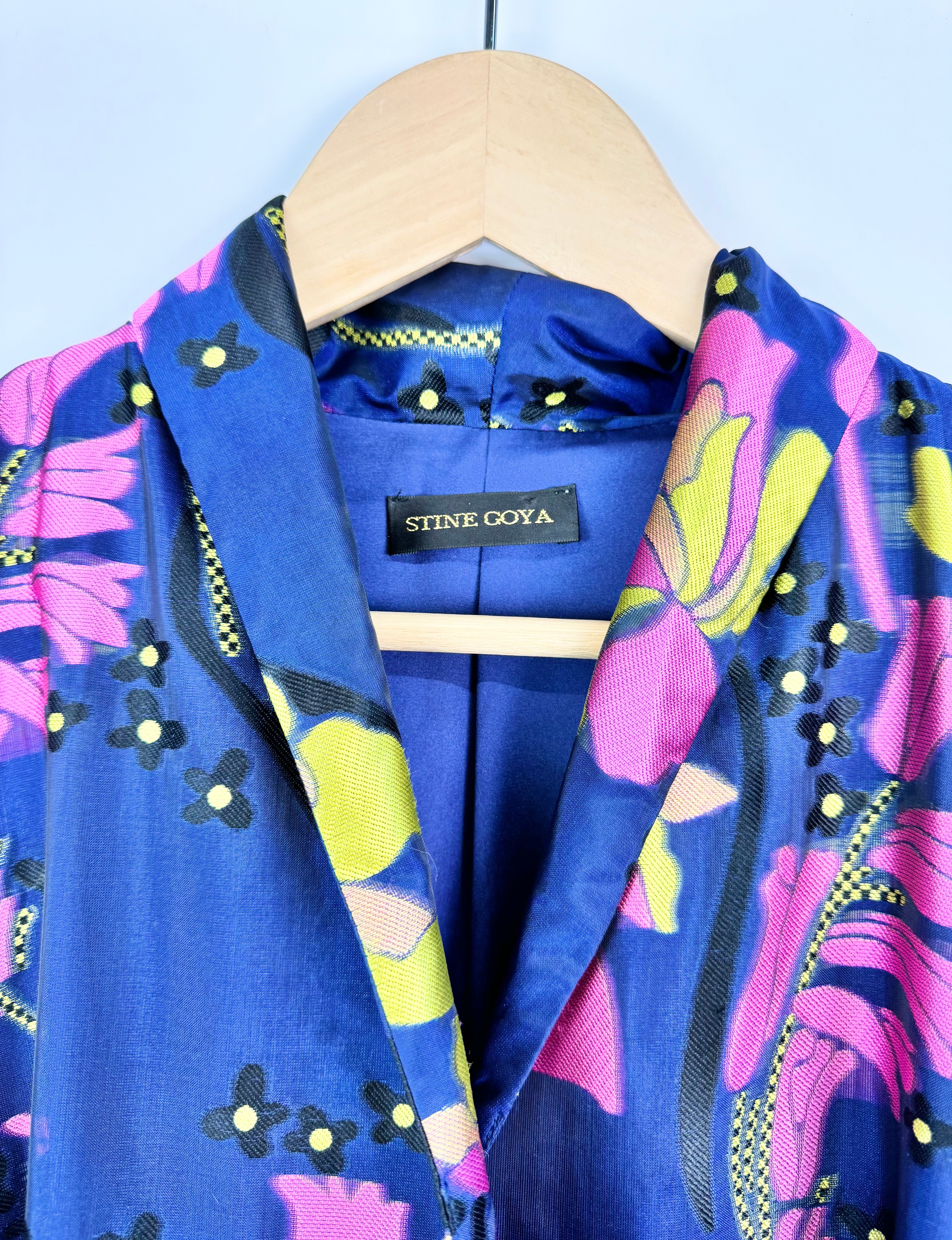 Blue jacket with colorful floral pattern on a hanger against a light blue background