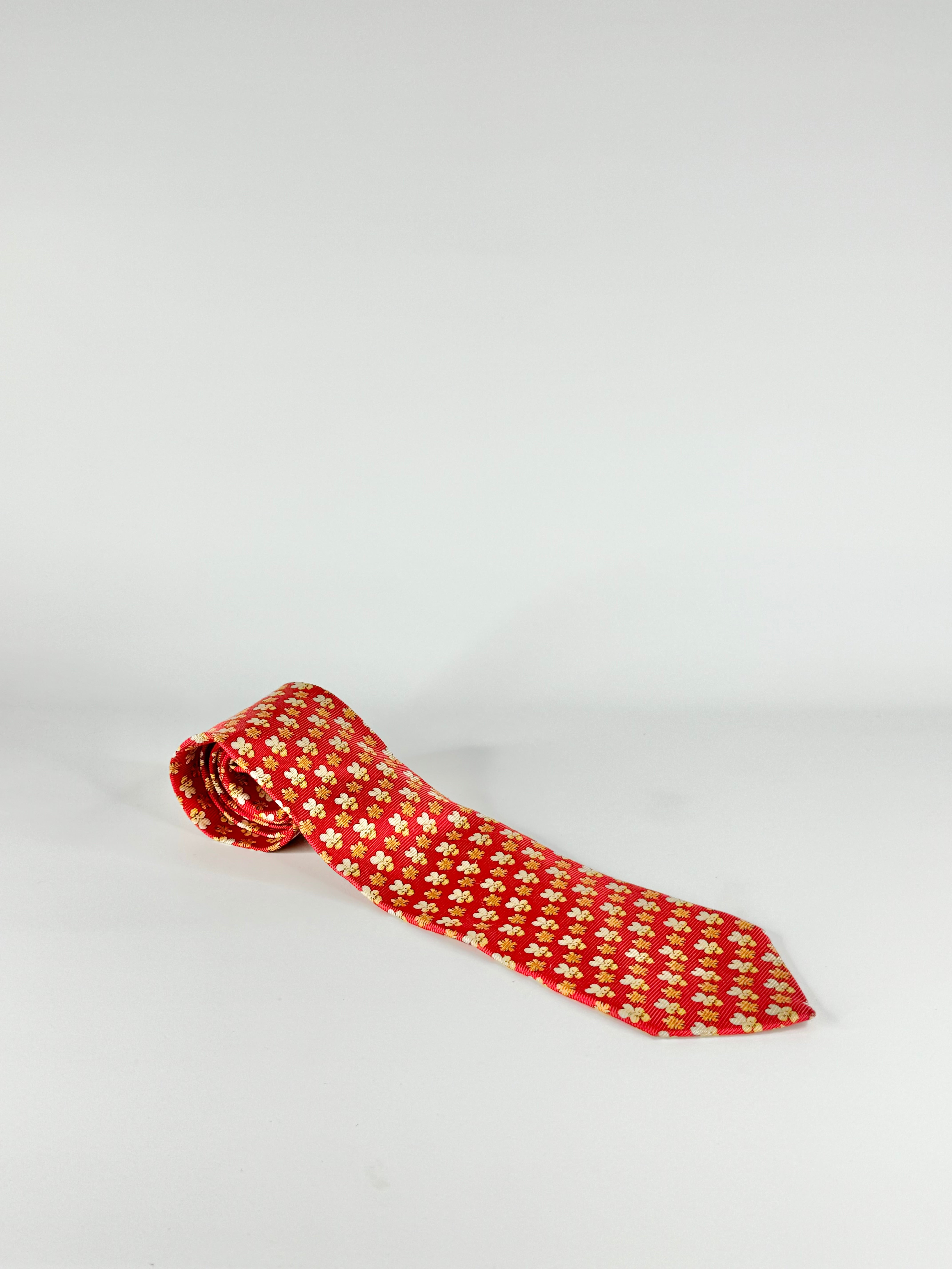 A bright red silk tie with an orange and gold floral pattern, displayed against a white background.