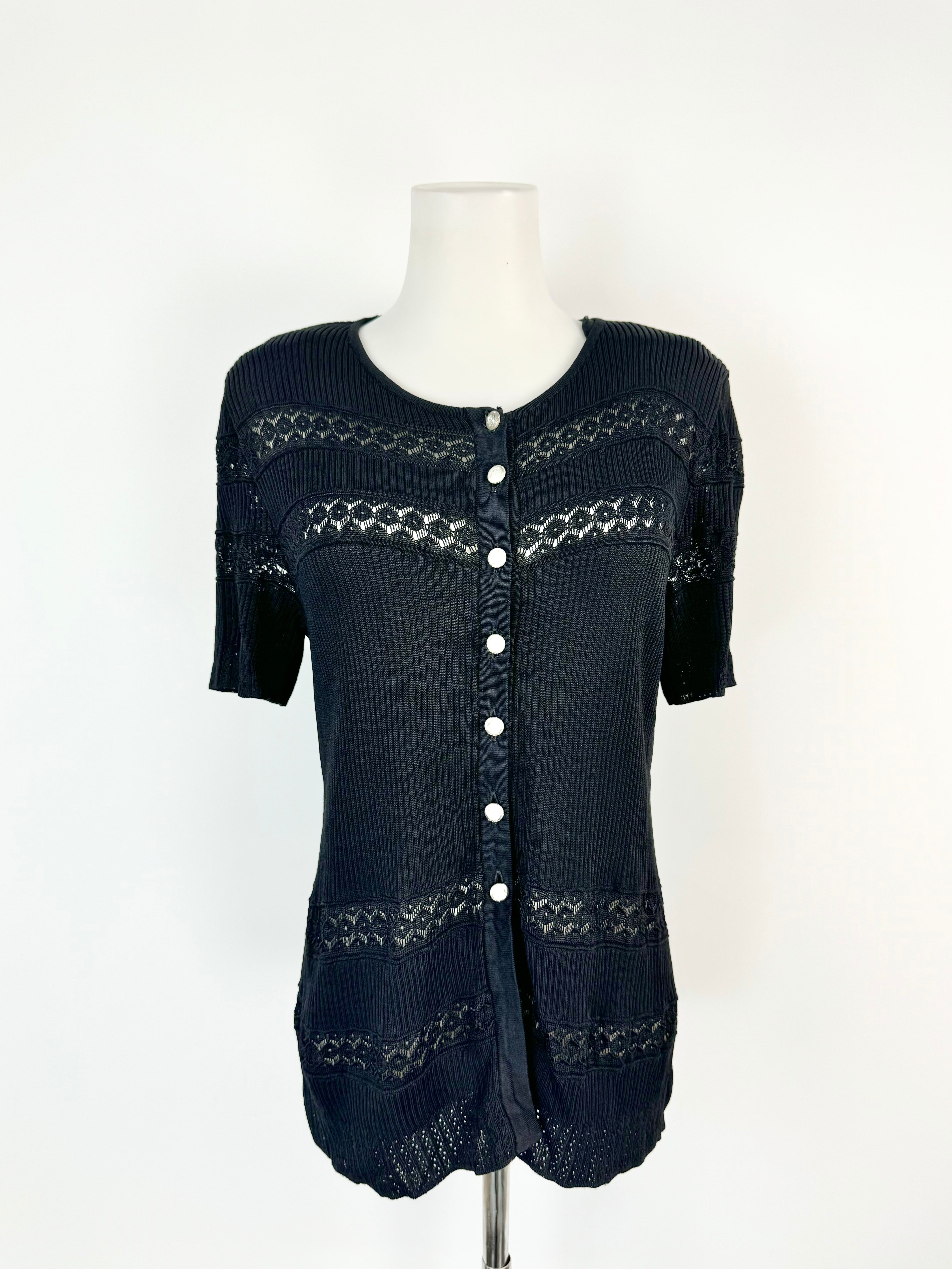 Black lace knit top with short sleeves, silver buttons, and padded shoulders displayed on a mannequin.