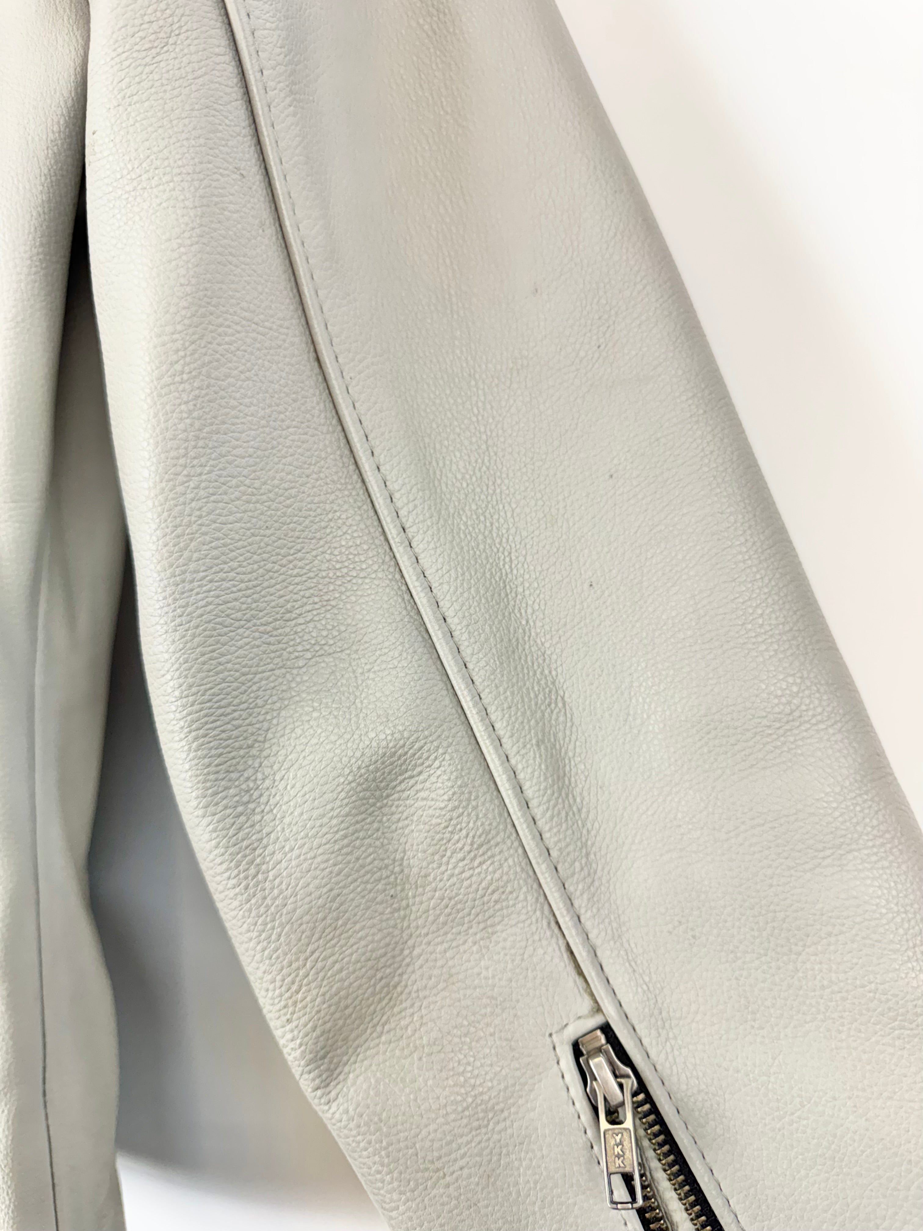 Close-up of a light gray leather jacket with a zipper on a white background